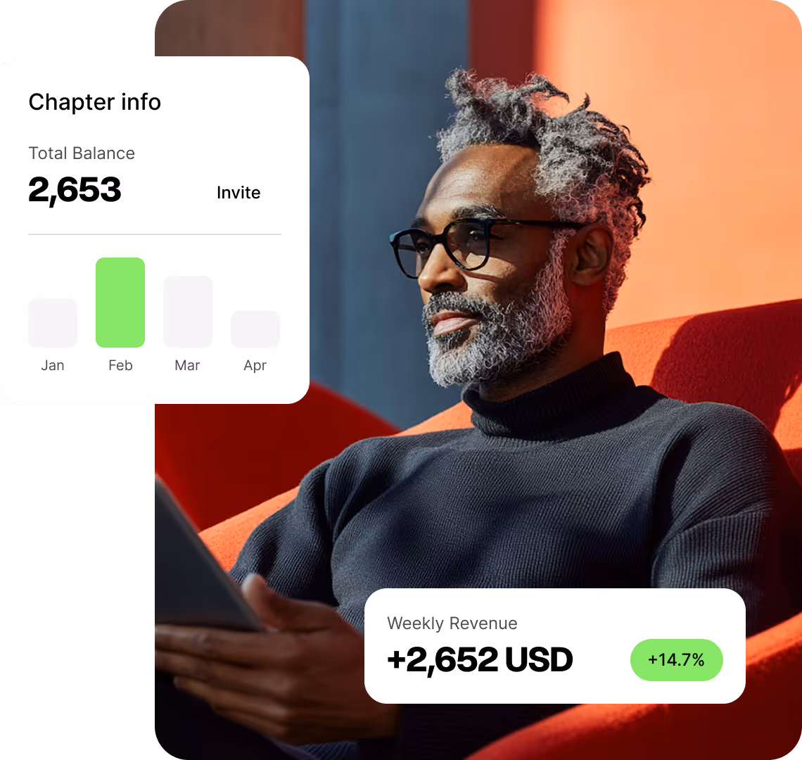 Man with gray hair and beard wearing glasses and a black turtleneck, sitting on an orange chair holding a tablet with financial stats overlays.
