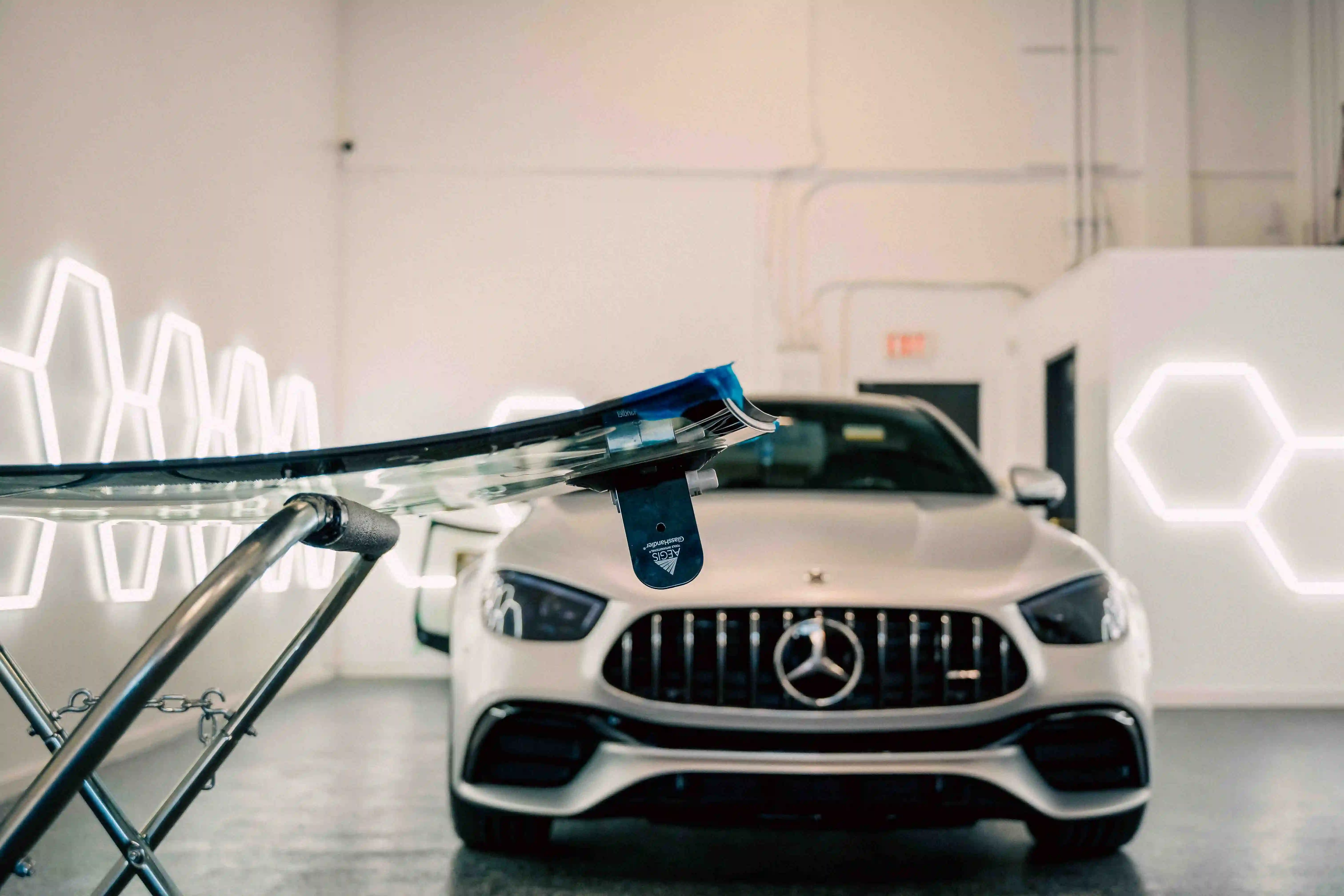 Windshield on stand with suction cups ready for installation, Mercedes-Benz in background