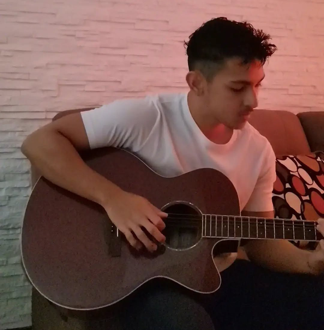 Enrique, AI developer at CRSS, playing guitar on his couch at home.