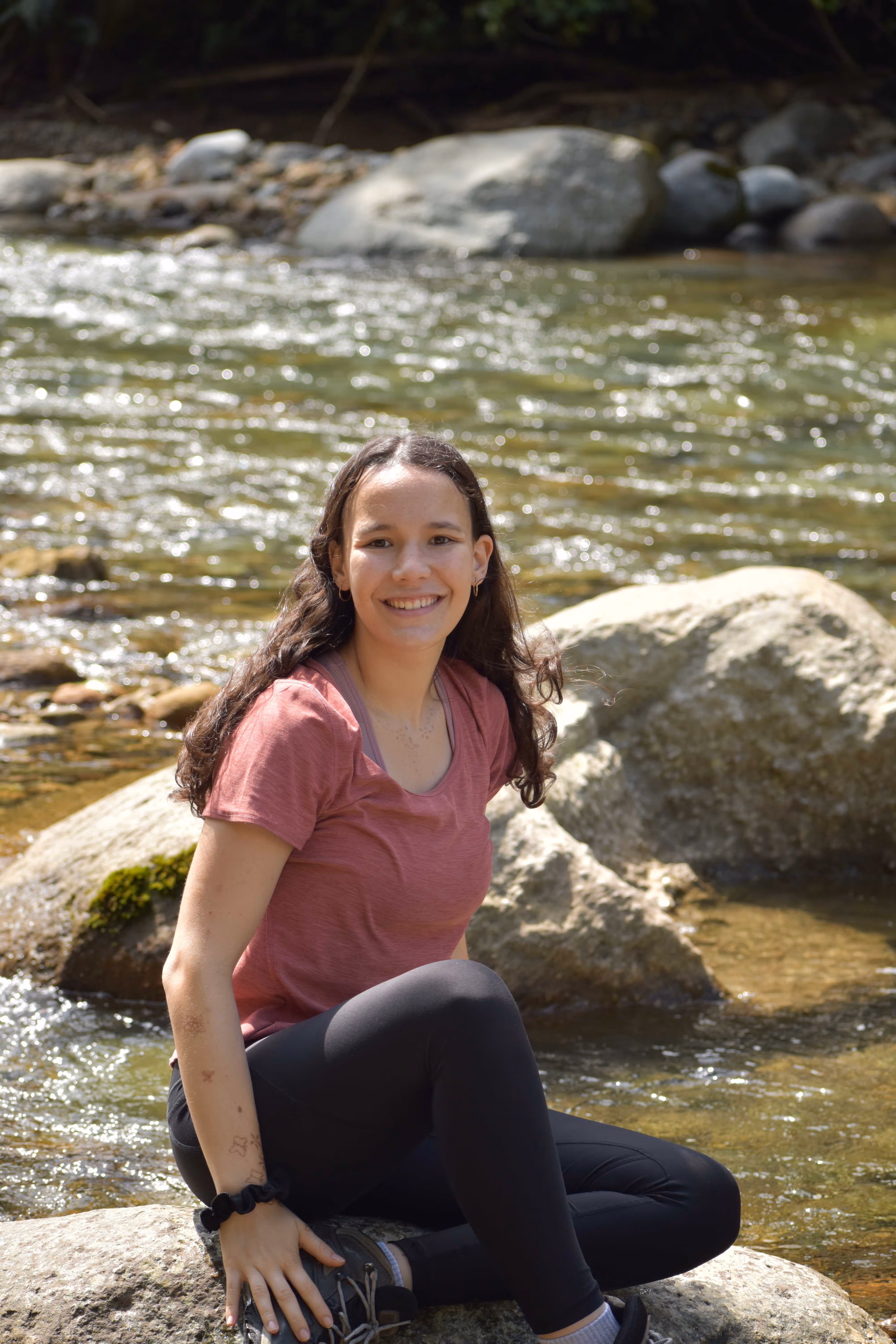 Emilia, AI developer at CRSS, smiling while standing in the middle of a peaceful river.