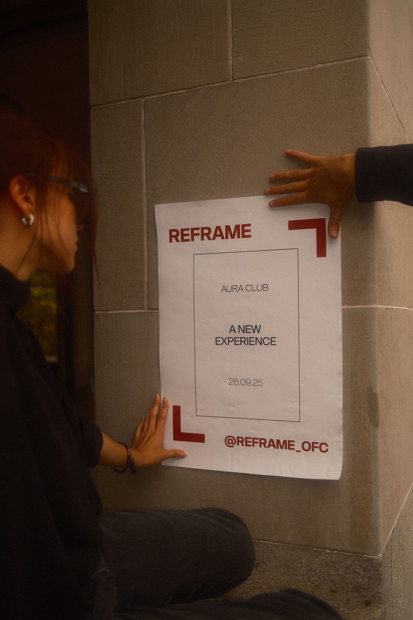 Zwei Personen befestigen ein REFRAME-Poster mit Event-Infos an einer Wand in Zürich.