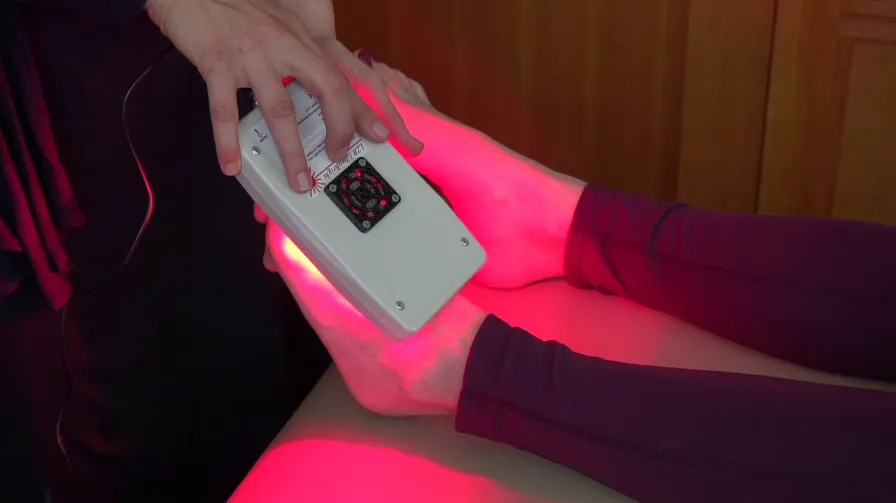 A device emitting red light therapy being applied to a person's leg, suggesting a therapeutic treatment to promote healing or improve circulation.