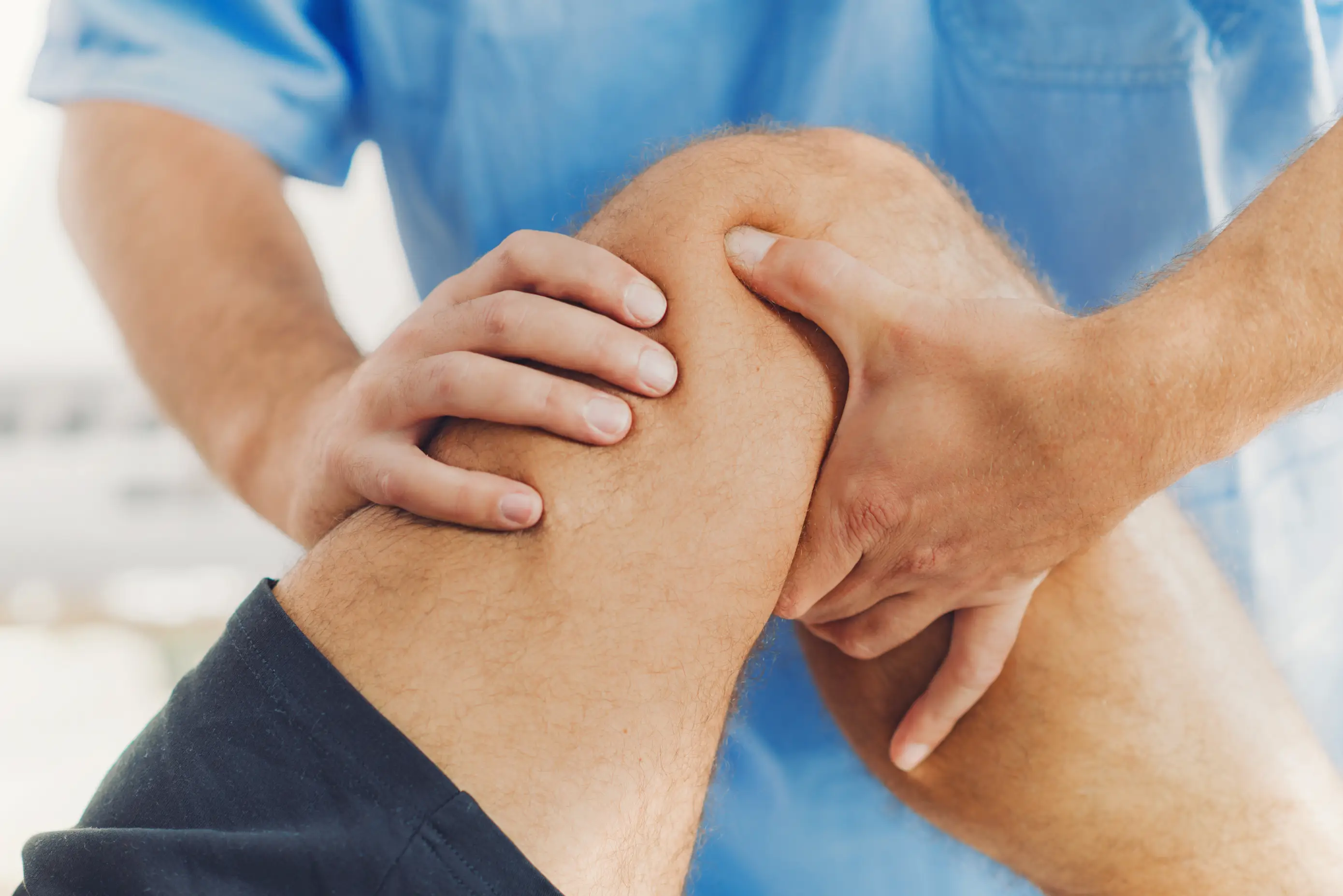Close-up of a healthcare professional examining and palpating a patient's knee joint, indicating a medical evaluation or treatment.