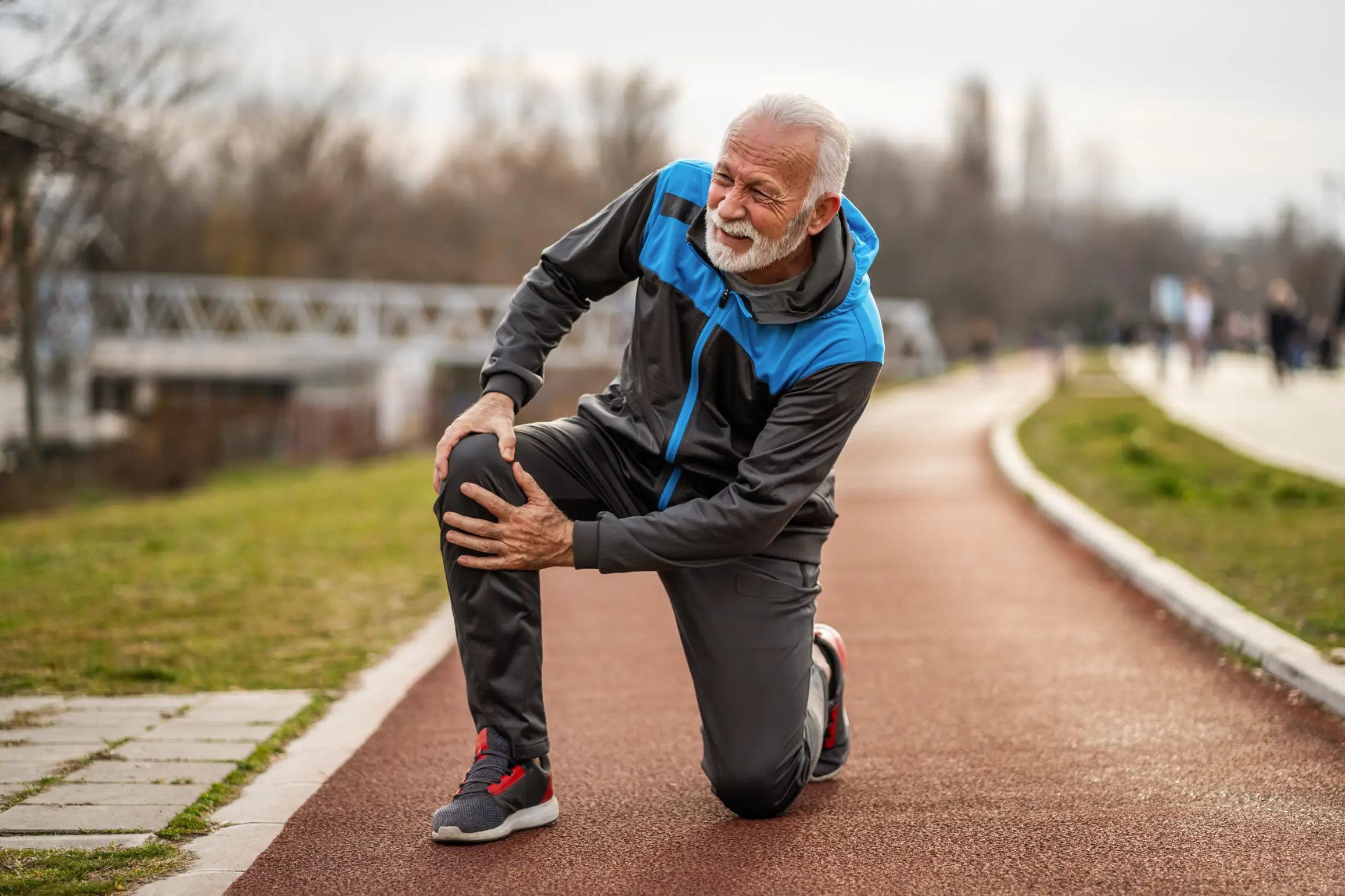 An elderly man outdoors, holding his knee with a pained expression, suggesting knee pain during exercise.