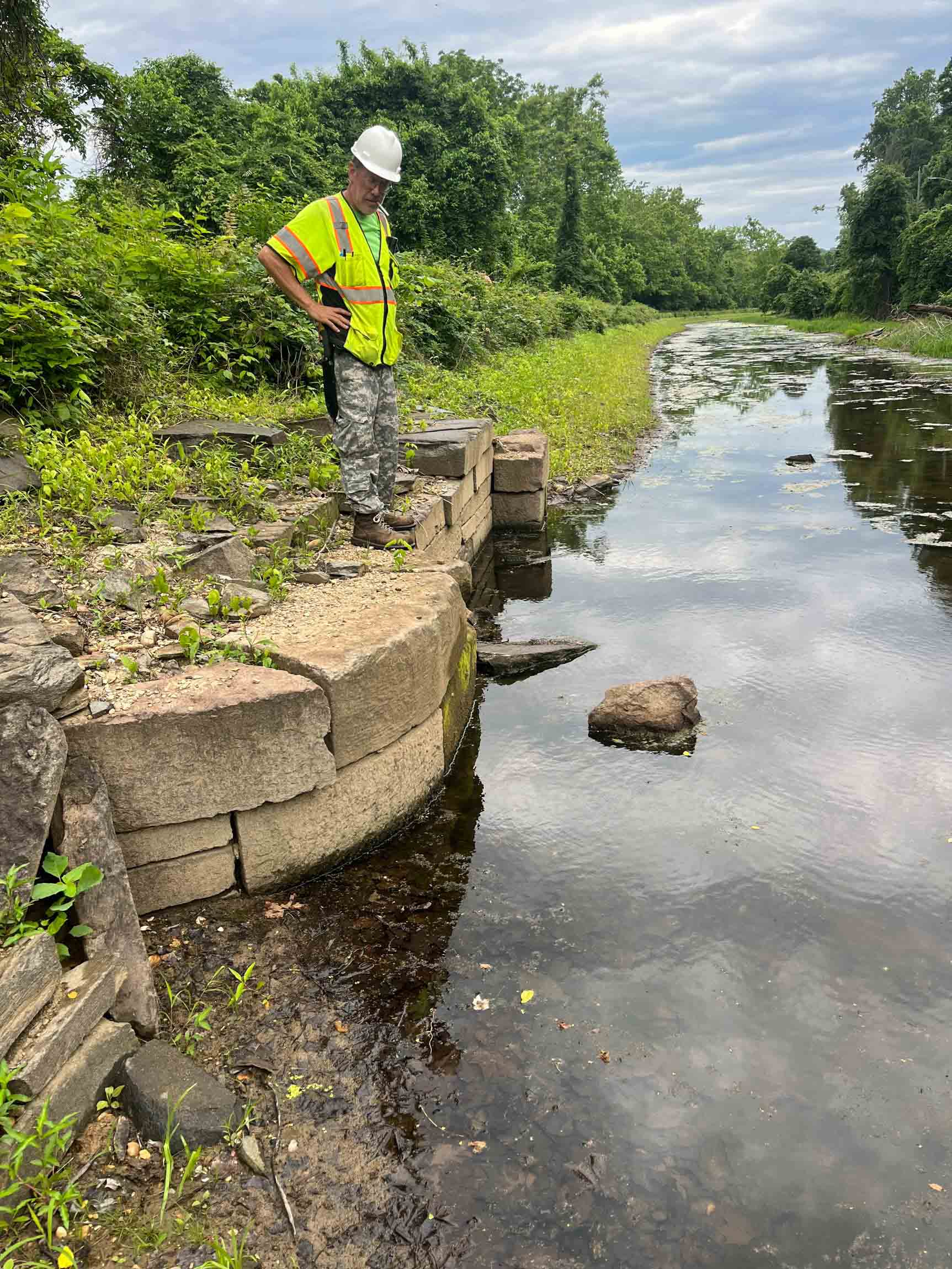 man standing next to waterway with hardhat on