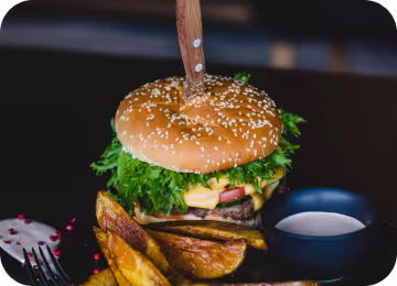 Burger with fried fries on black plate with sauce on the side