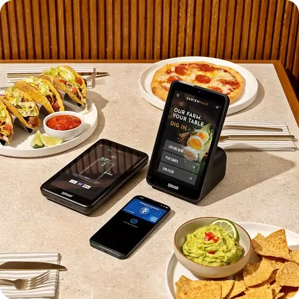 Table with tacos, pizza, guacamole with chips, and three Ziosk tabletop tablets, one displaying a menu.