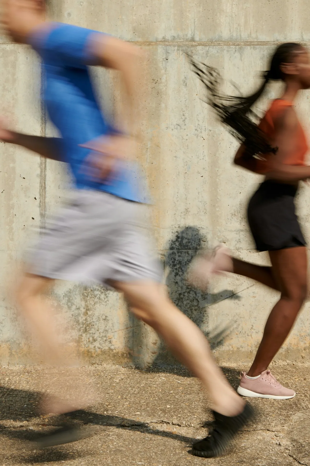 Two athletes running past a concrete wall in motion blur
