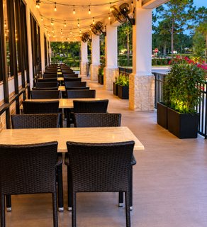 Outdoor dining area with tables and wicker chairs under string lights along a walkway with plants.