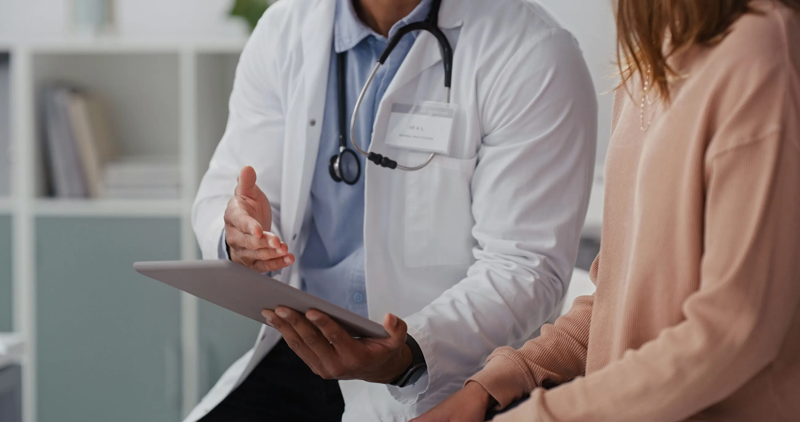 Doctor in white coat with stethoscope consulting a patient using a tablet.