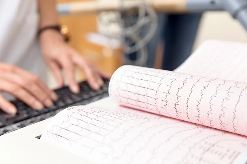A doctor typing on a keyboard in front of a tablet of cardiogram results