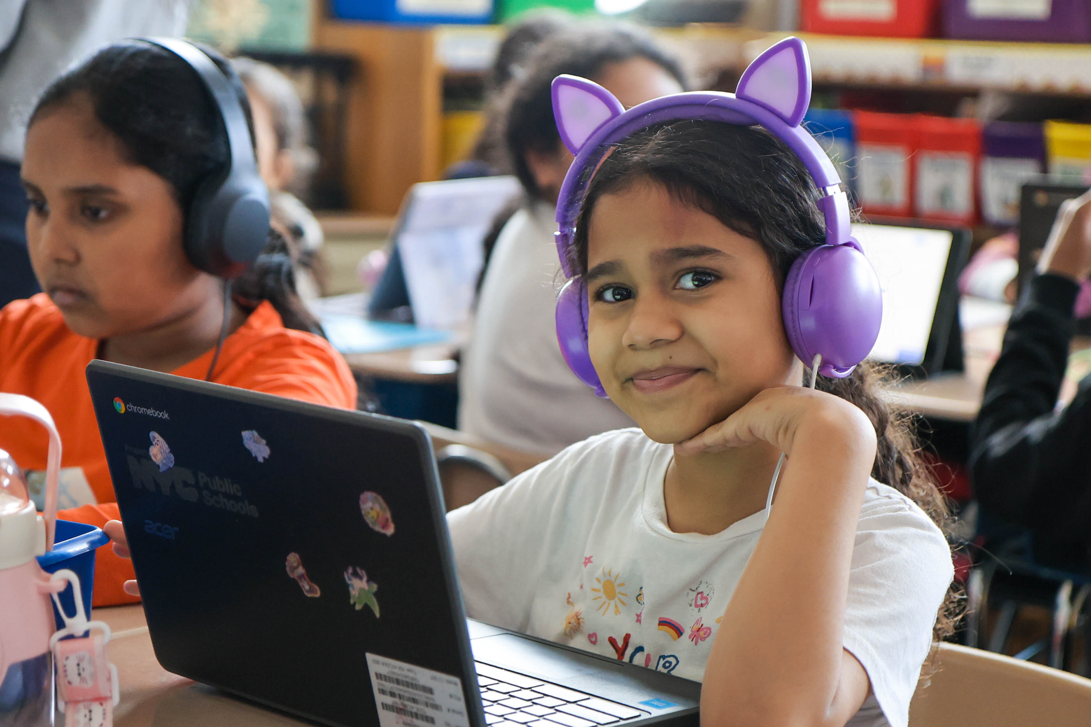 Student wearing purple cat-ear headphones uses NYC Public Schools Chromebook