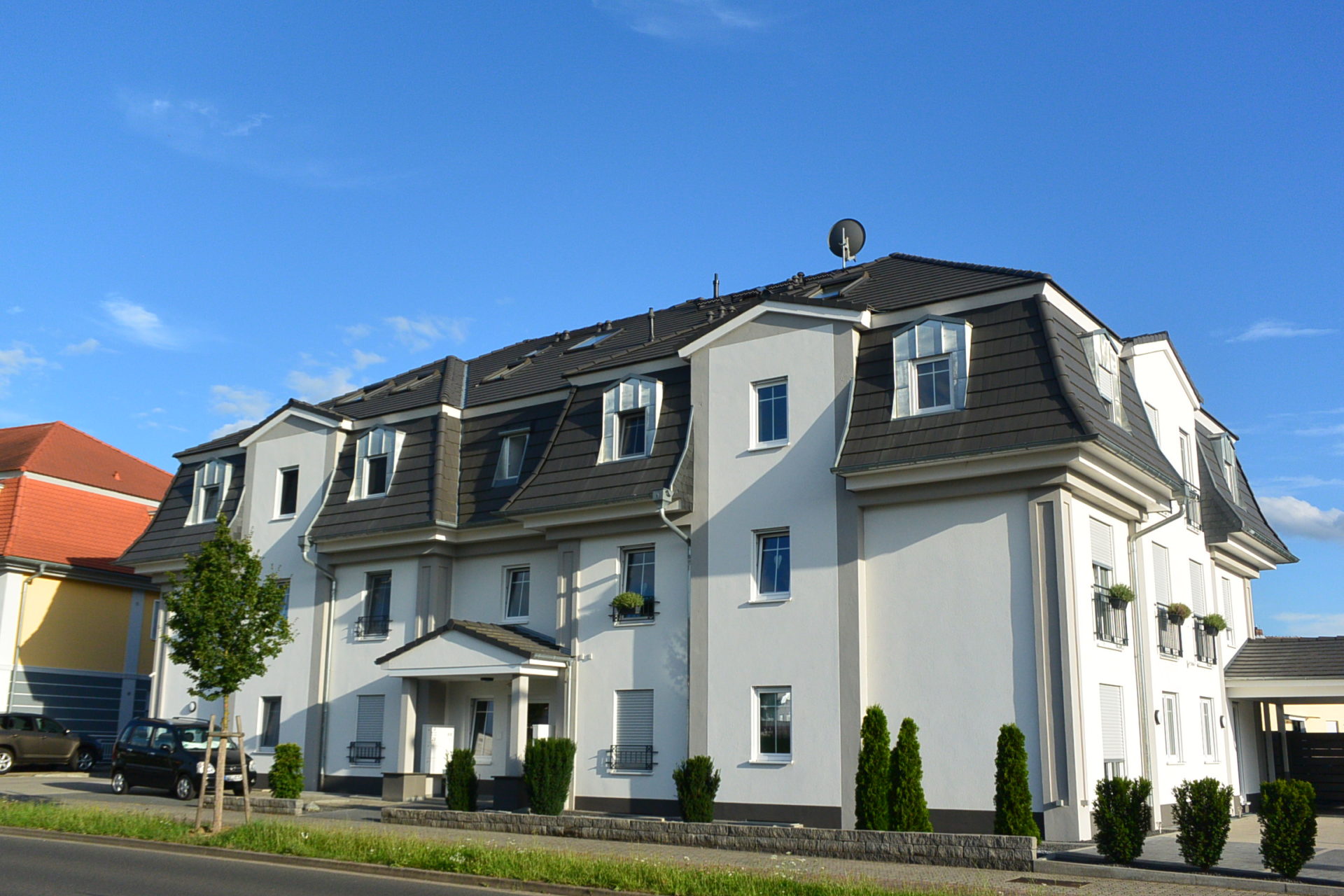 Modern white apartment building with dark mansard roof under a clear blue sky.
