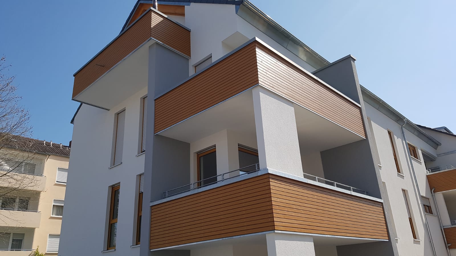 Modern white apartment building with wooden panel balconies under a clear blue sky.