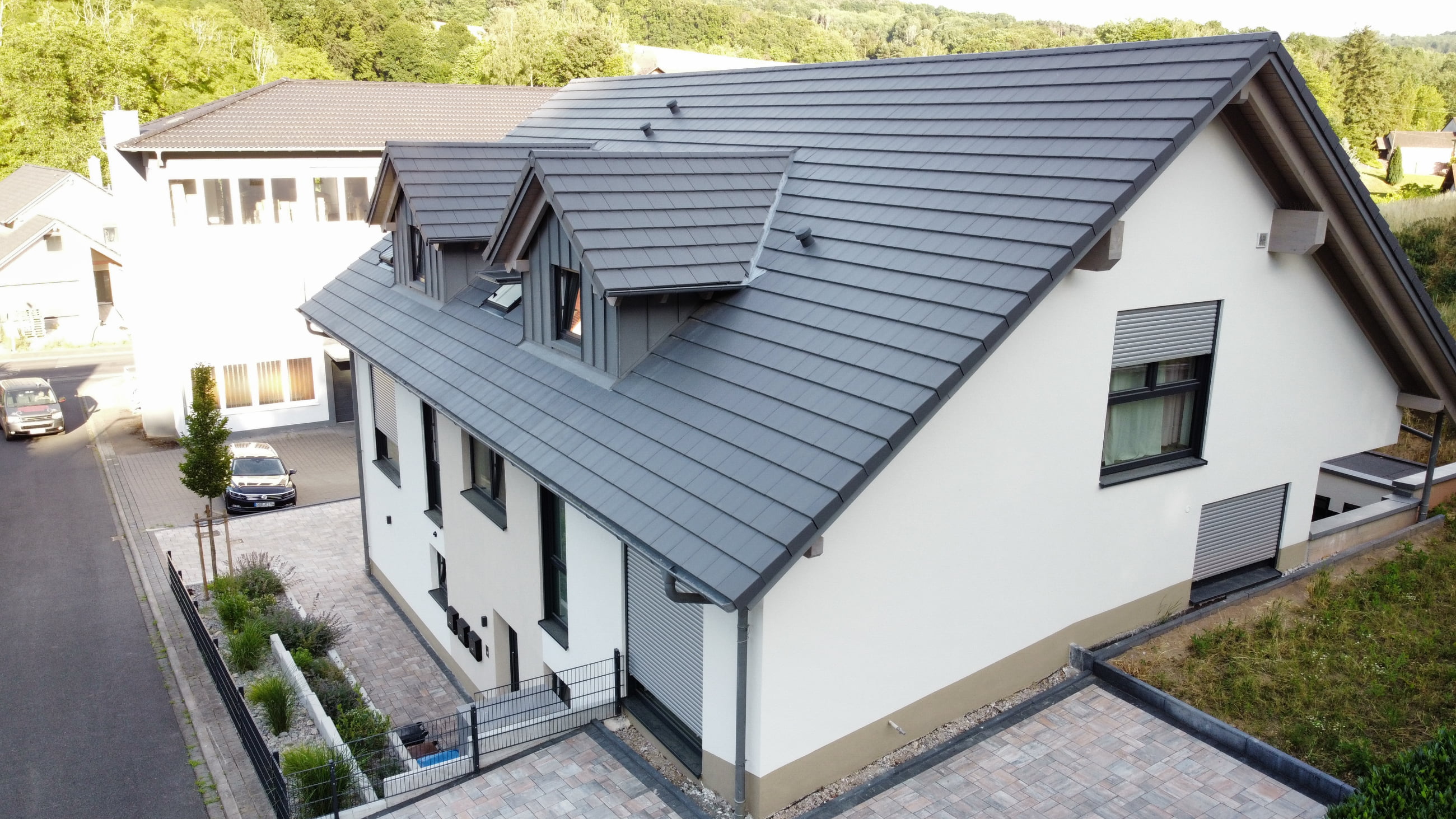 Modern two-story house with white walls, gray roof tiles, and closed window shutters in a suburban neighborhood.