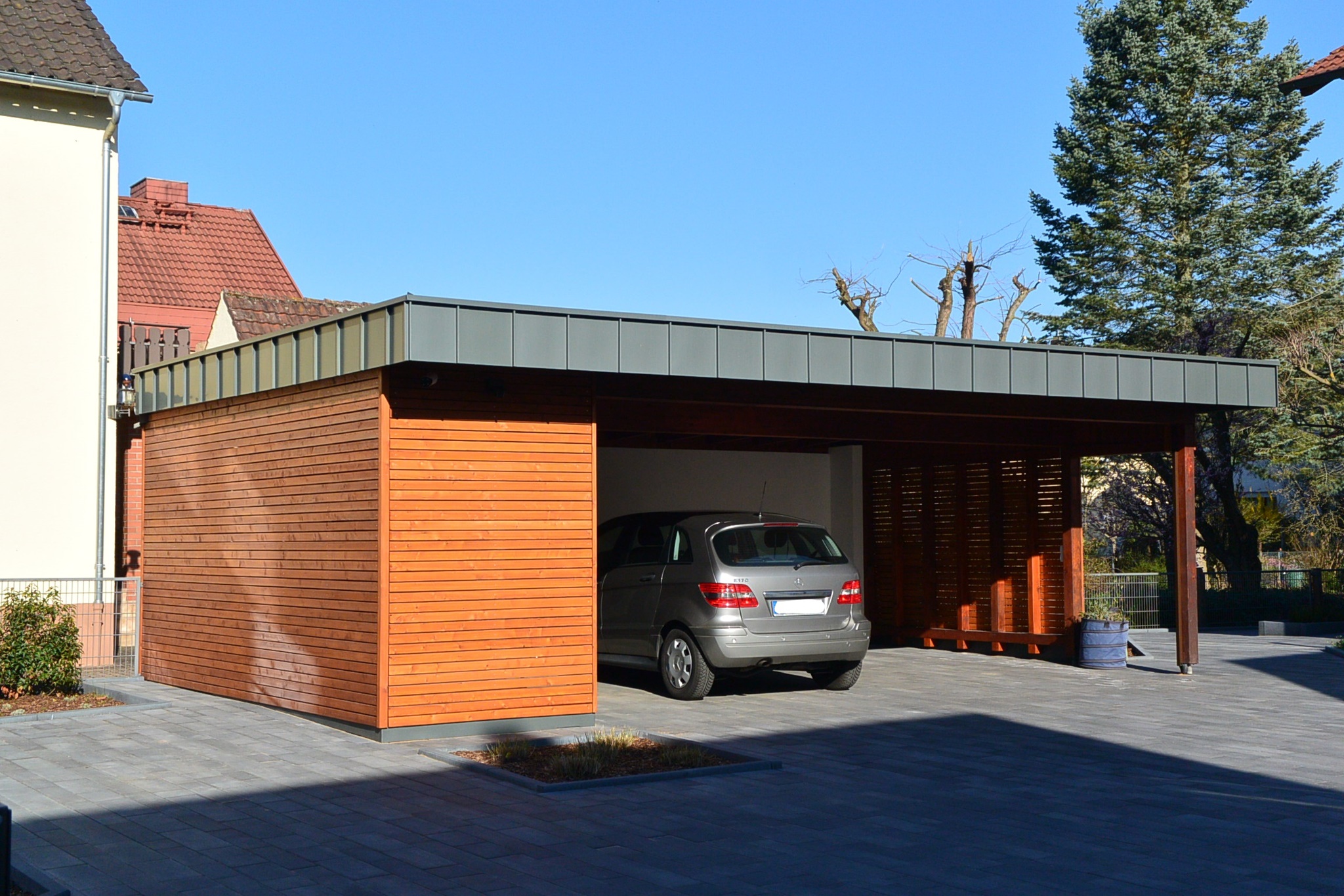 Silver car parked inside a modern wooden carport with a flat roof on a sunny day.