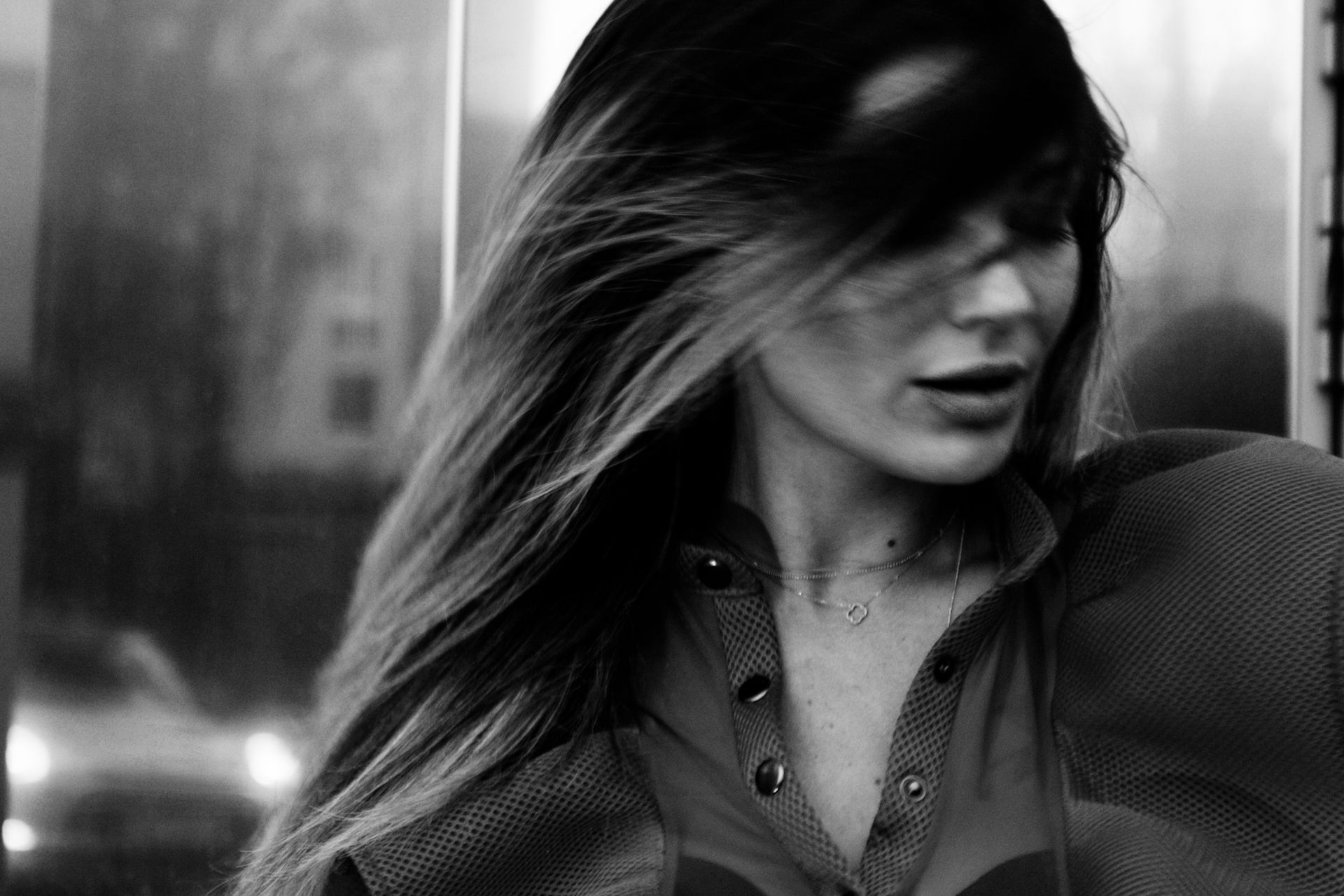 Black and white close-up of a woman with long hair partially covering her face, wearing a textured top and delicate necklace.