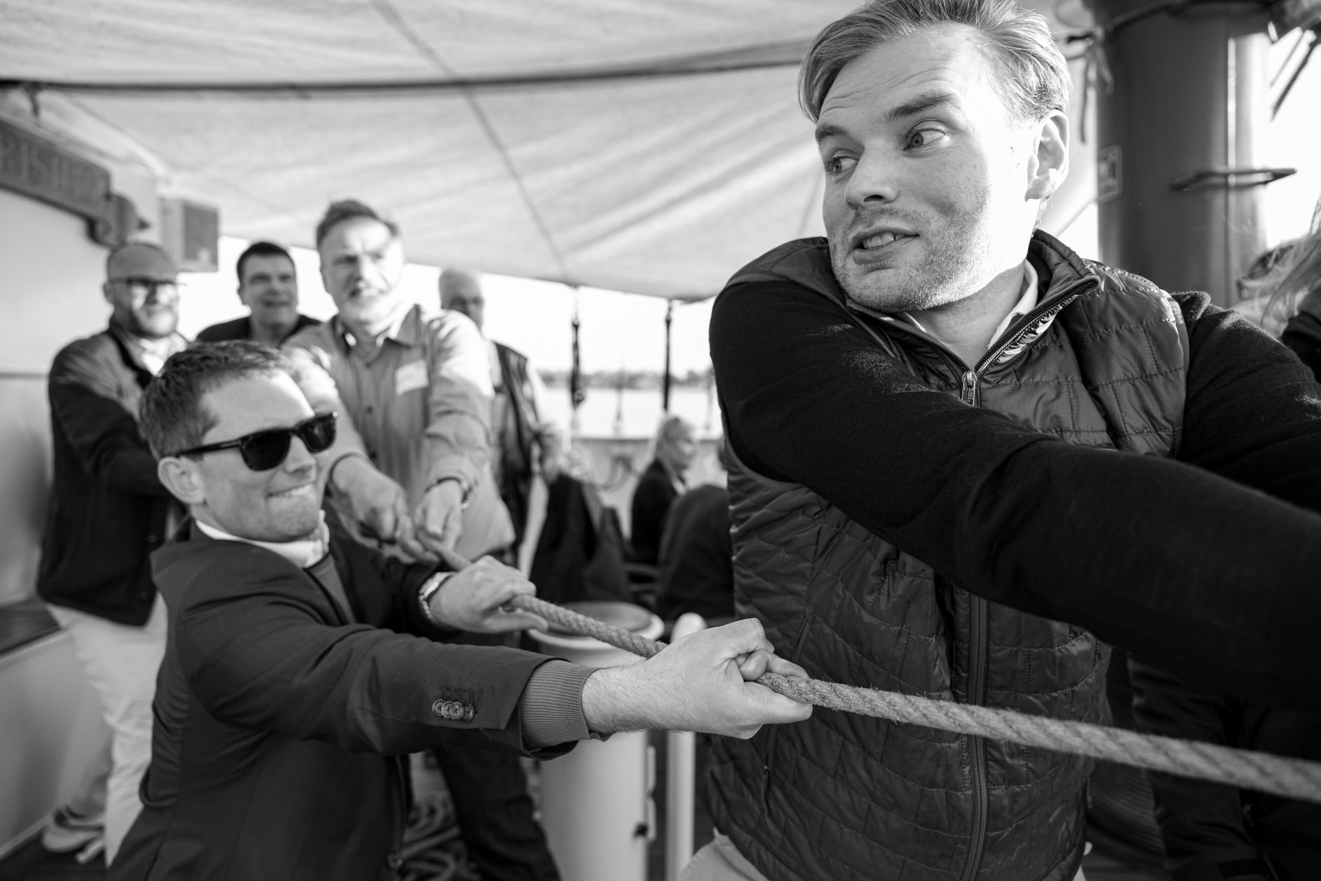 A group of men engaged in a tug-of-war on a boat, pulling a thick rope with focused expressions.