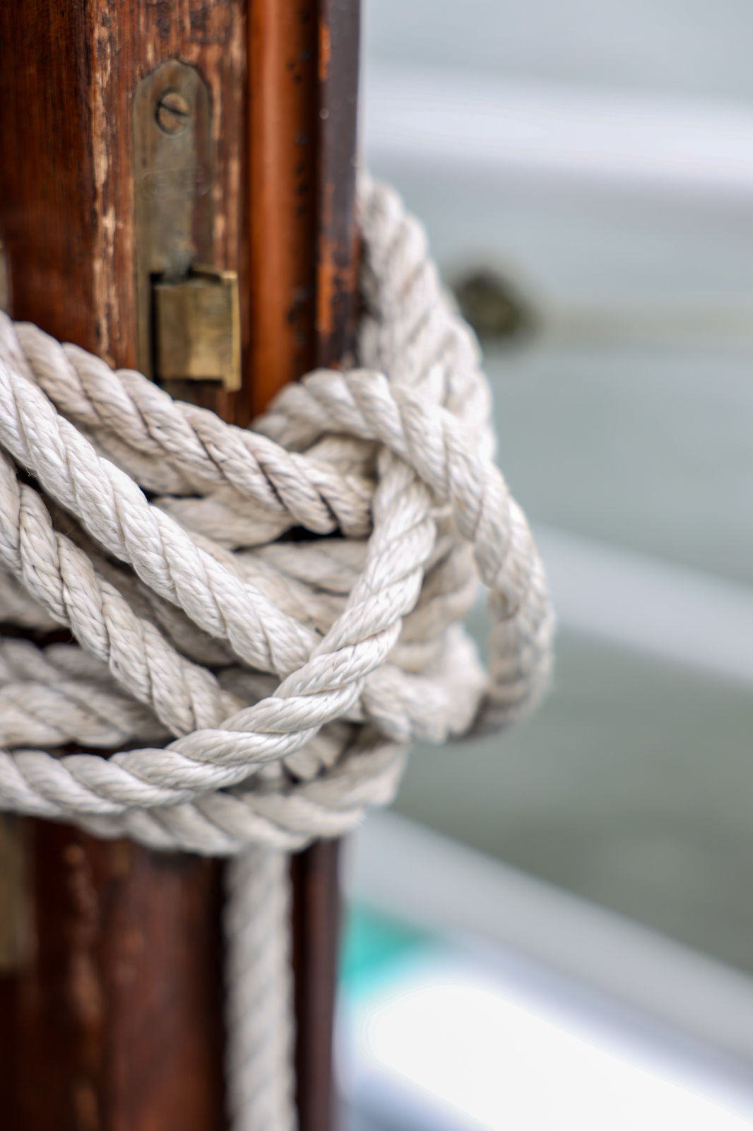 Close-up of a thick white rope tied tightly around a wooden post on a boat with blurred water in the background.