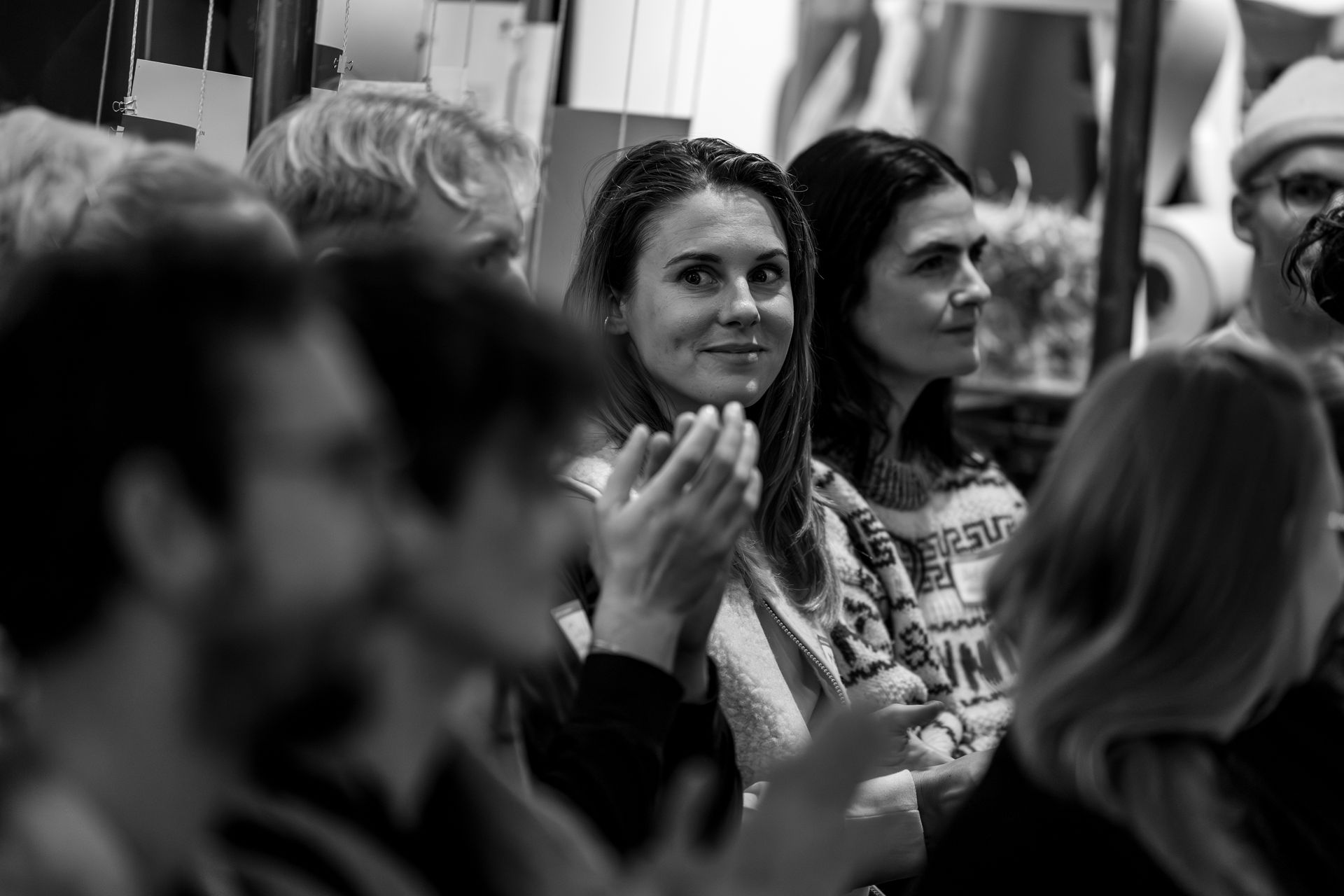 Black and white photo of a group of people seated, with a woman in the center smiling and clapping.