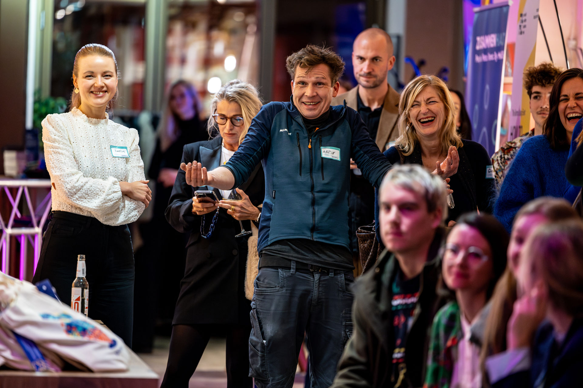 A group of diverse adults at an indoor social event, smiling and engaging with each other, some holding drinks.