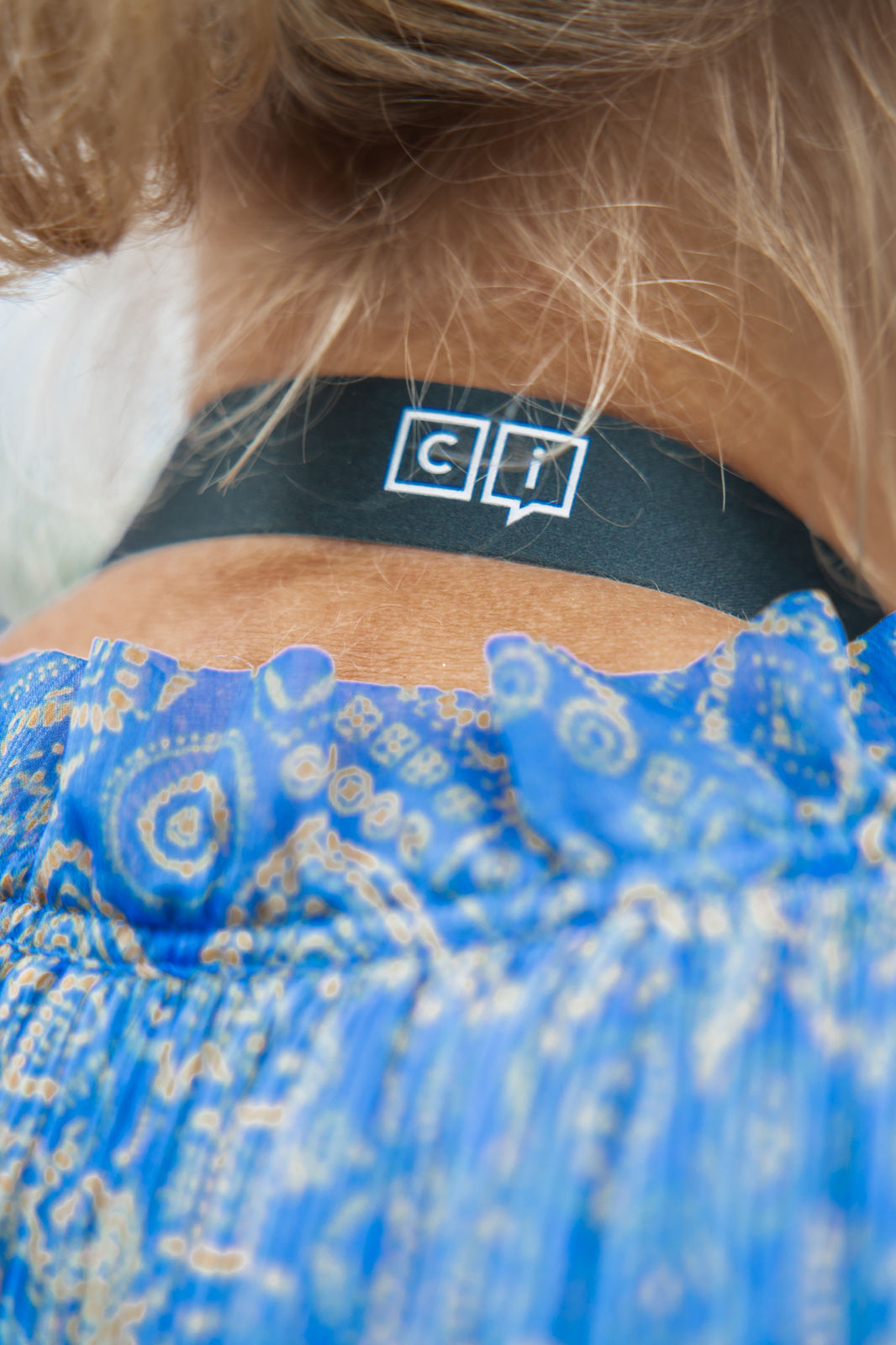Back of a person's neck wearing a black band with white 'ci' logo above a blue patterned garment.