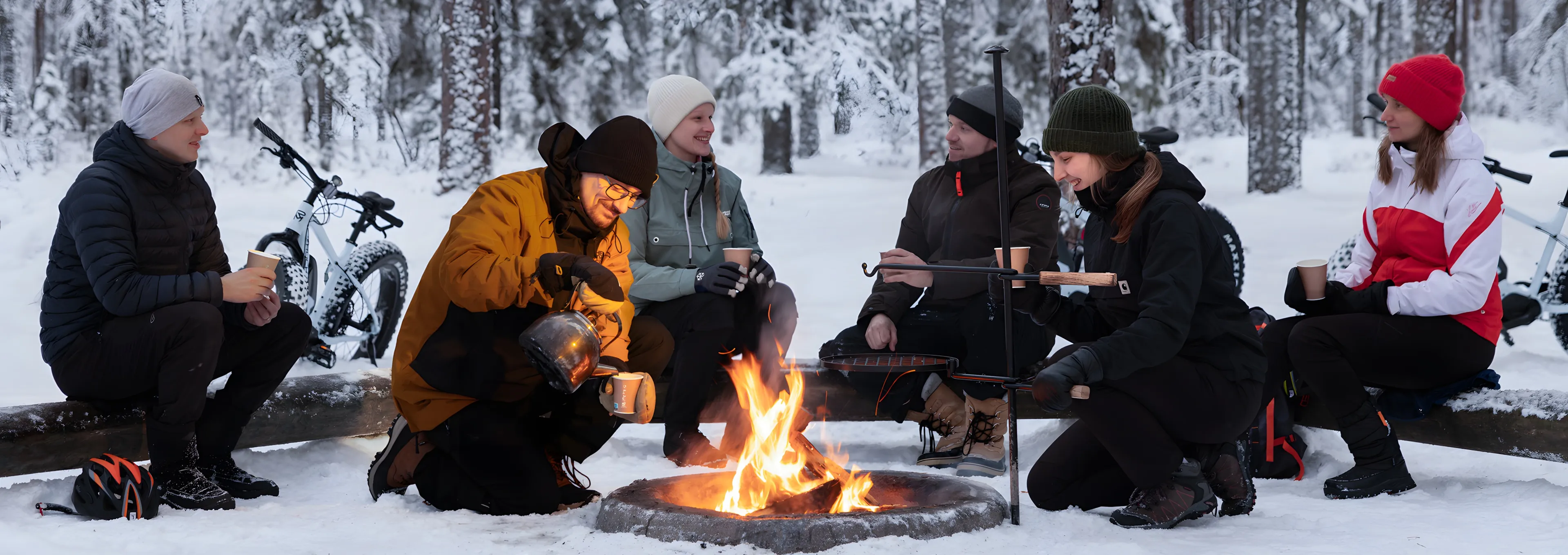 Henkilöitä talvisessa metsässä nuotion äärellä