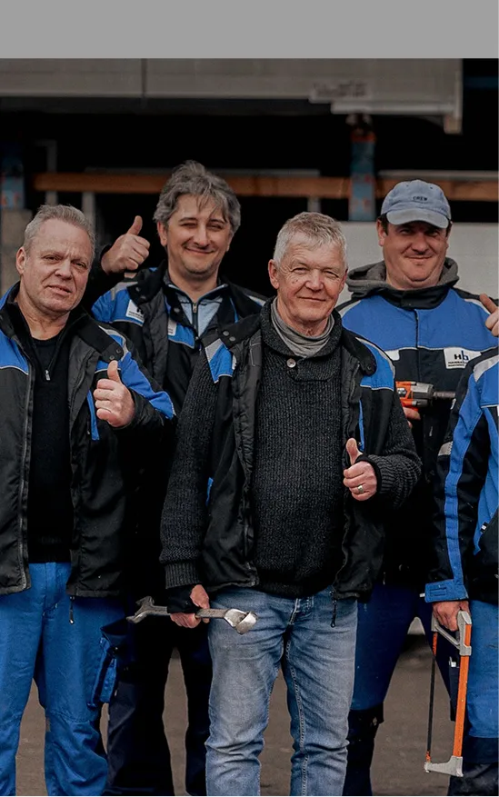 Fünf Handwerker in Arbeitskleidung stehen nah beieinander und zeigen Daumen hoch, einer hält einen Schraubenschlüssel.