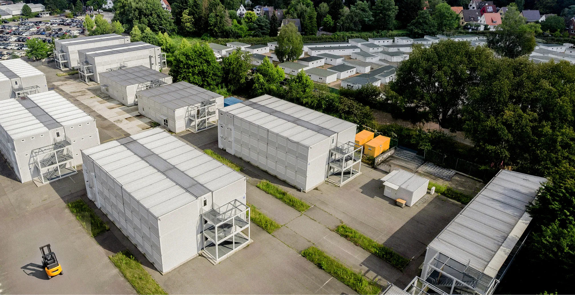 Luftaufnahme eines Industriegebiets mit mehreren weißen, modularen Lagergebäuden und einem gelben Gabelstapler auf der Straße.