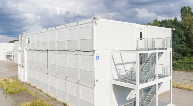 Modulare, zwei-geschossige, weiße Büro- und Verwaltungscontainer mit Außentreppe bei bewölktem Himmel.