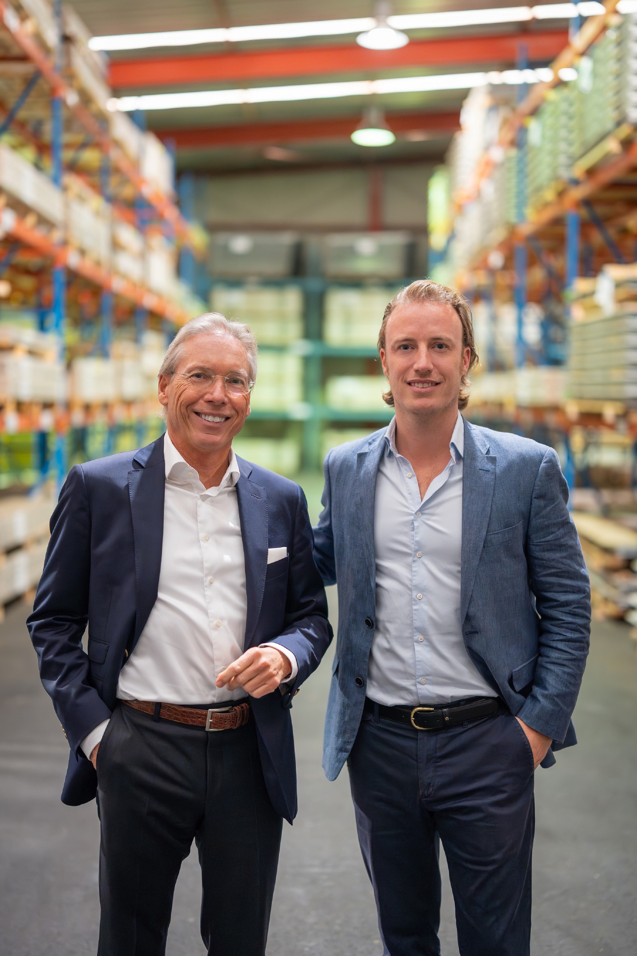 Zwei Männer im Businessoutfit stehen in einem Lagerhaus mit Regalen voller Kartons und Lagerschränken.