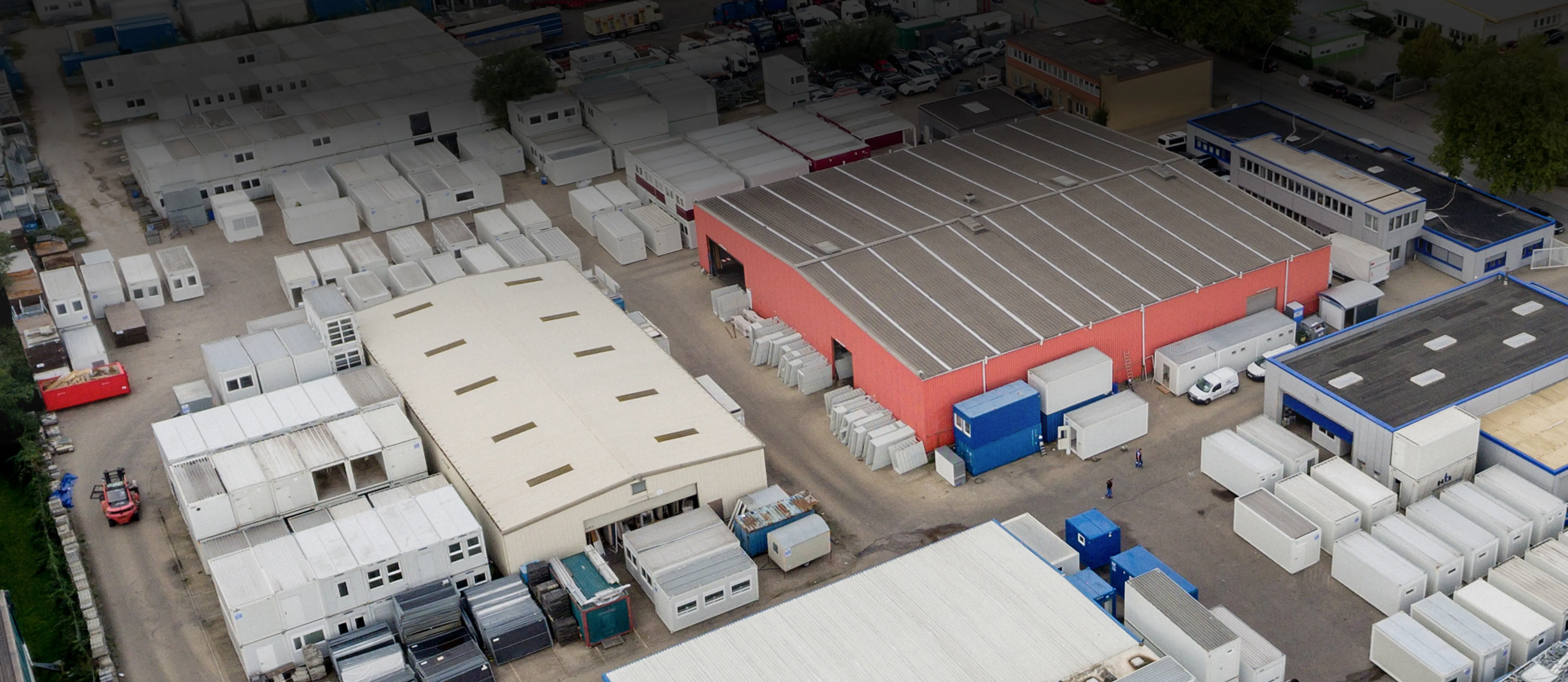 Luftaufnahme eines Industriegebiets mit mehreren Lagerhallen und zahlreichen weißen, modularen Maschinencontainern.