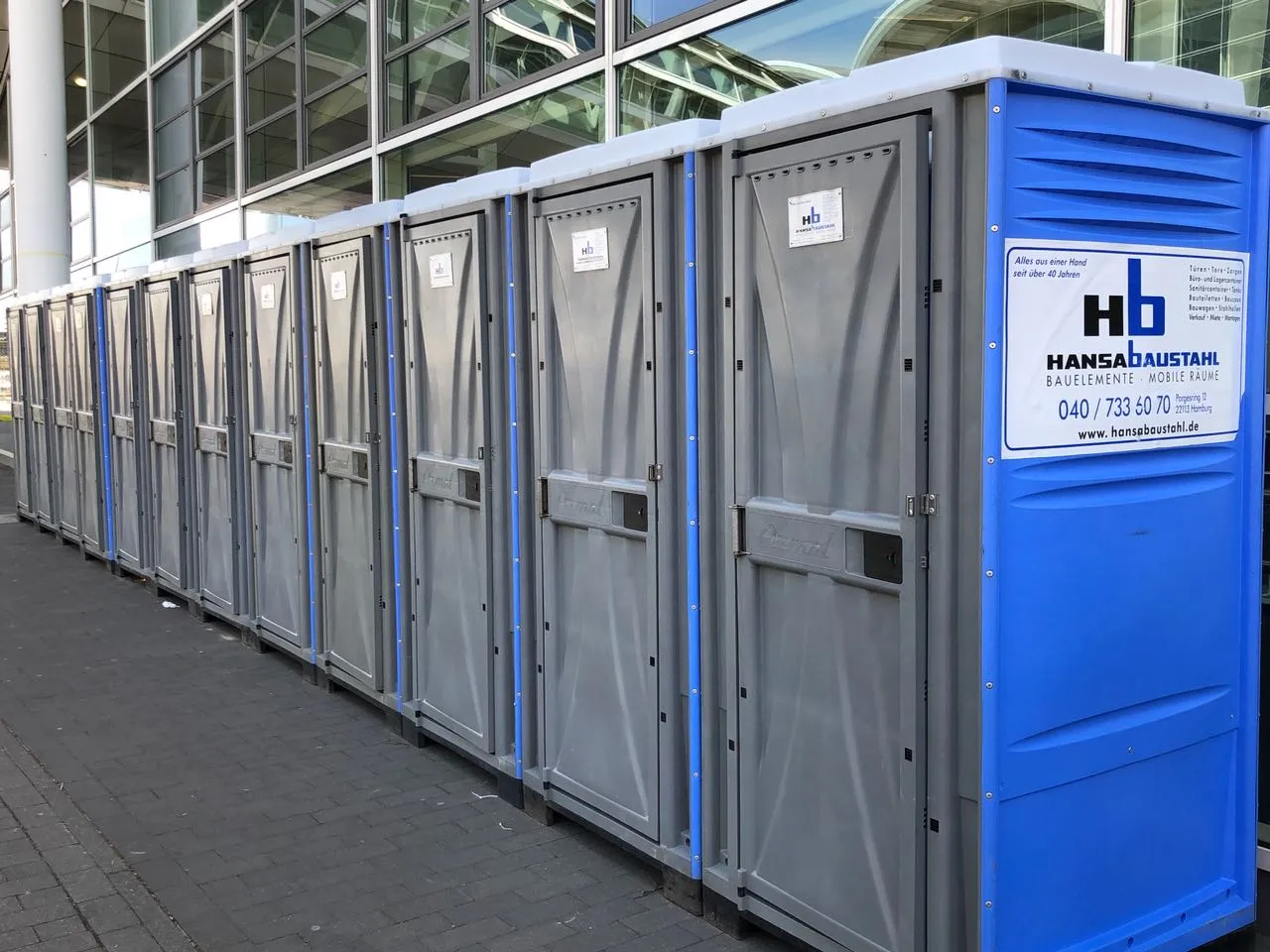 Reihe von grauen und blauen mobilen Toilettenkabinen vor einem modernen Gebäude.