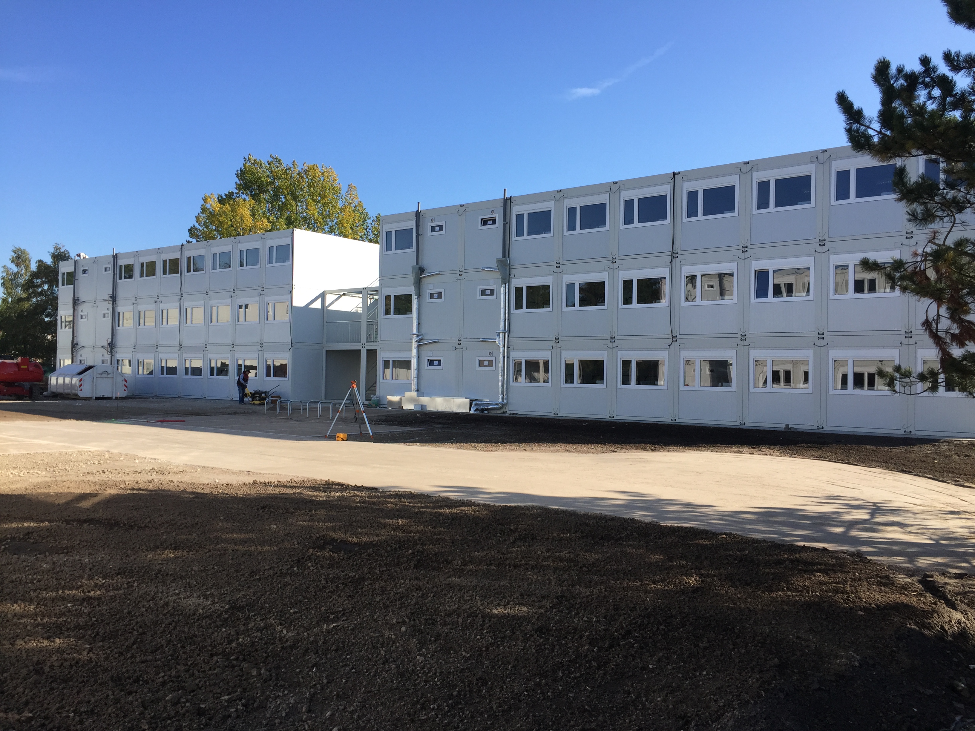 Mehrstöckige weiße Wohncontaineranlage mit zahlreichen Fenstern unter klarem blauem Himmel.