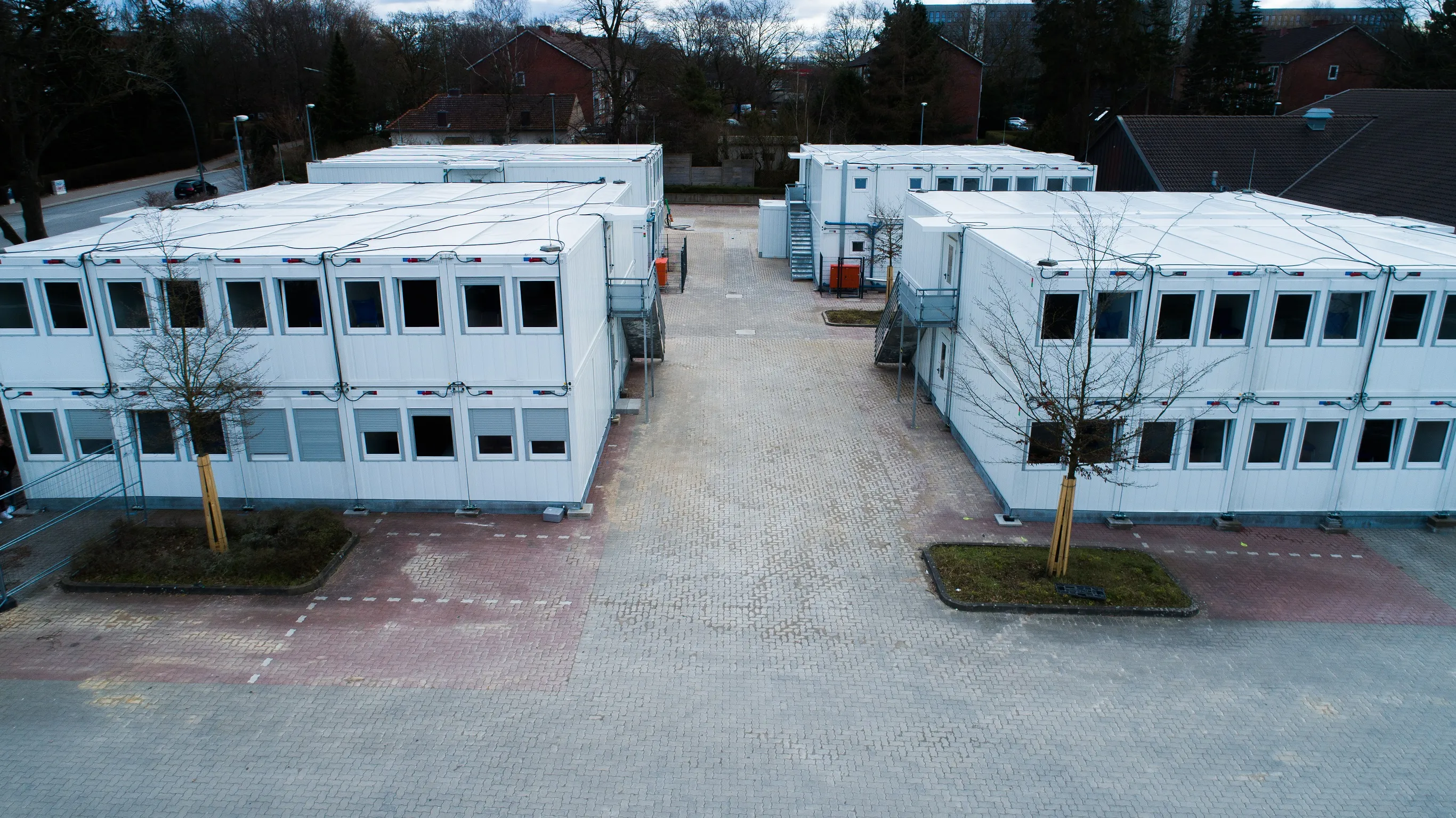 Zwei zweistöckige weiße modulare Gebäude mit mehreren Fenstern, die einen gepflasterten Innenhof mit Bäumen umgeben.