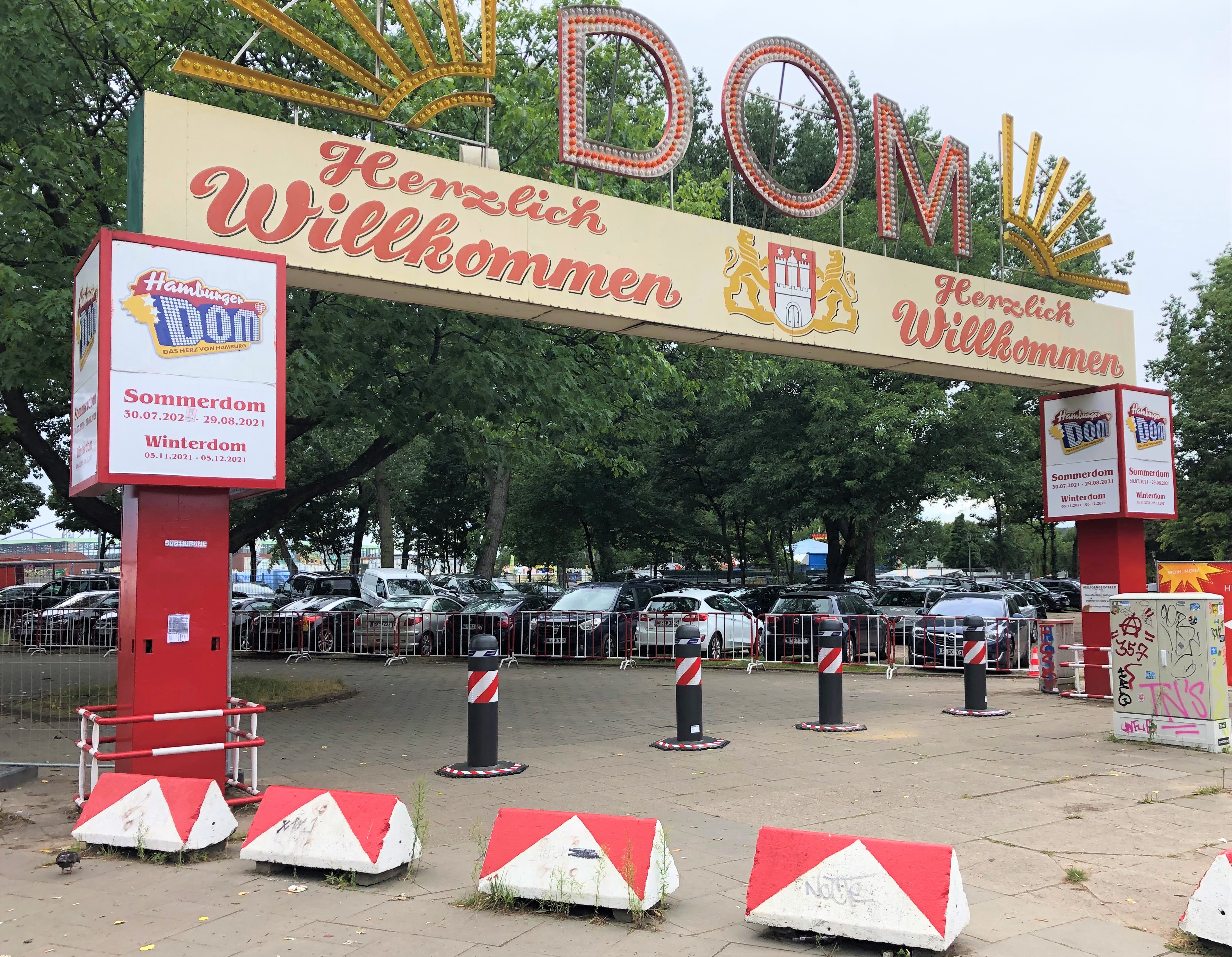 Eingang zum Hamburger DOM mit einem großen Schild, auf dem ‚Herzlich Willkommen‘ steht, und Informationstafeln zu Sommer- und Winterdom.