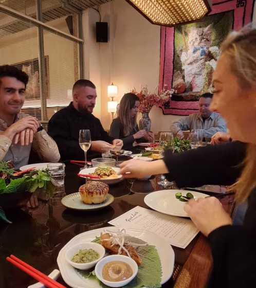 Group of people seated around a dining table enjoying a meal with assorted dishes and drinks.