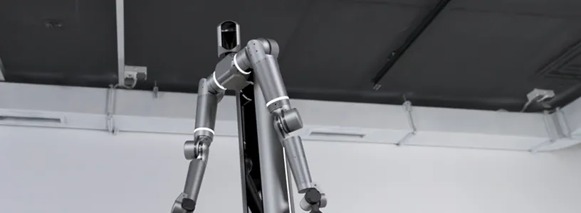 Metallic humanoid robot standing indoors against a dark ceiling background.