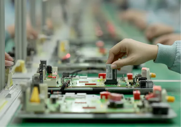 Gloved hand inserting a RAM module into a circuit board on an electronics assembly line.