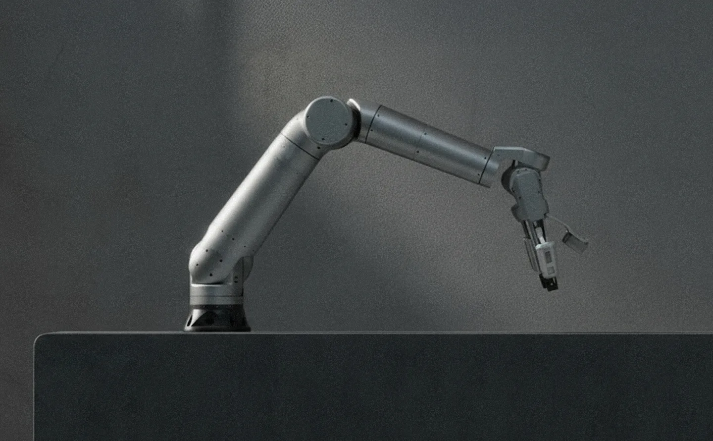 Metallic robotic arm with a claw-like gripper mounted on a dark surface against a plain dark background.