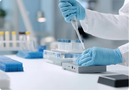Scientist wearing blue gloves using a pipette to transfer liquid into a test device in a laboratory.