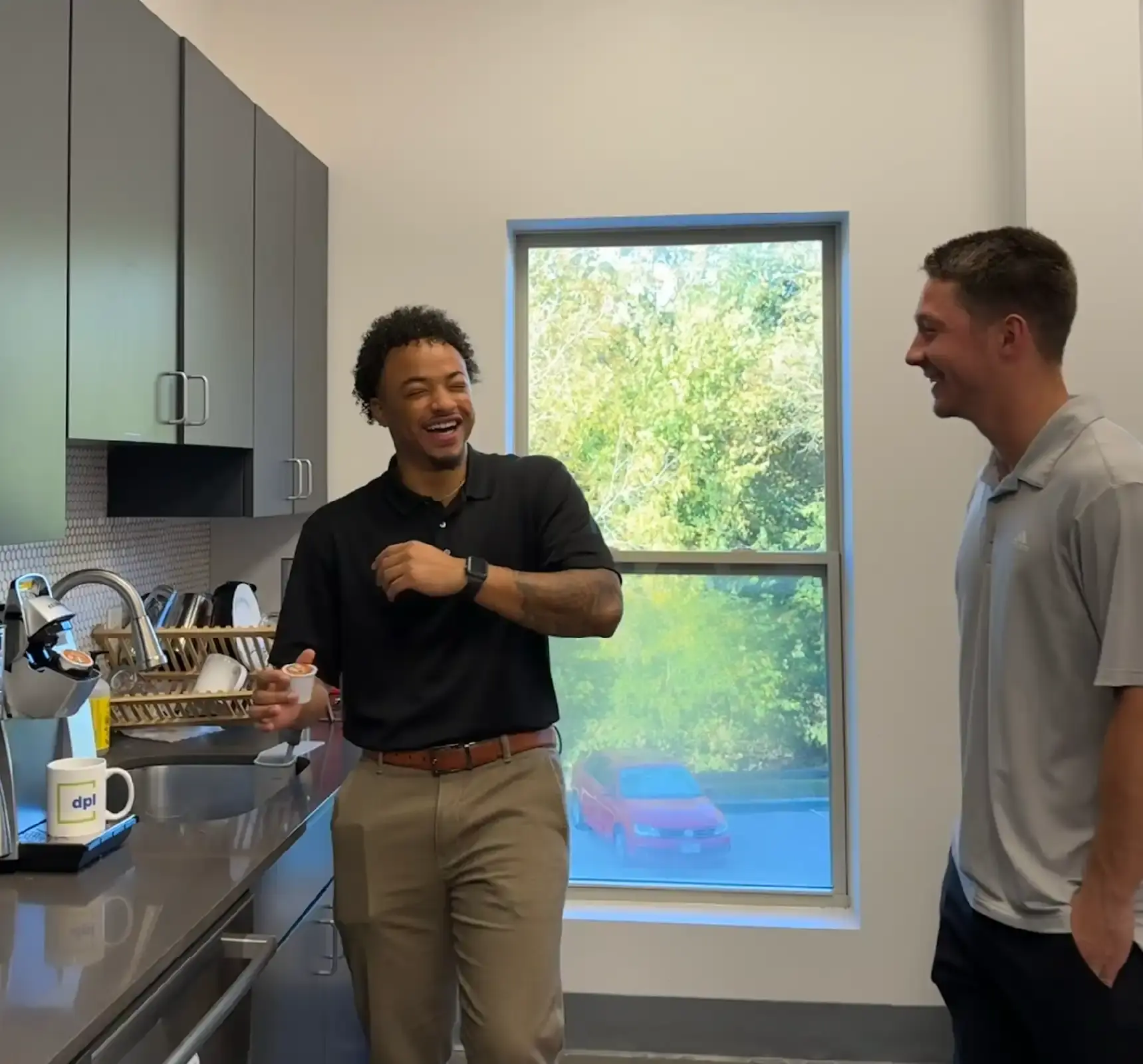 Two coworkers laughing in office kitchen.