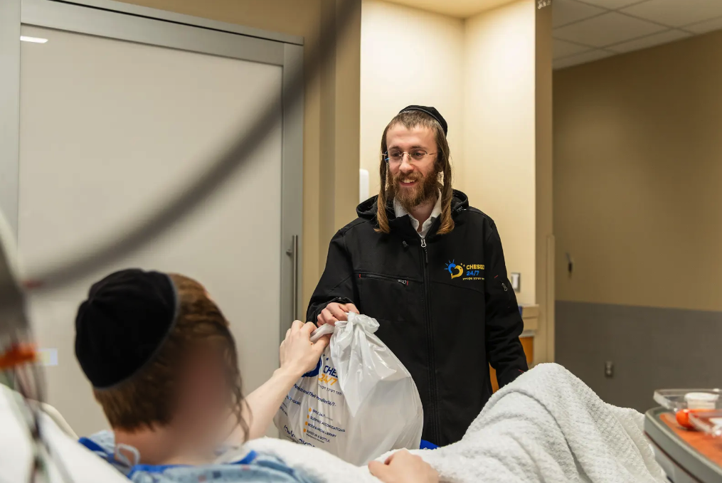 Smile 24/7 volunteer delivering a care package to a patient in a hospital room as part of Chesed 24/7’s emotional support program
