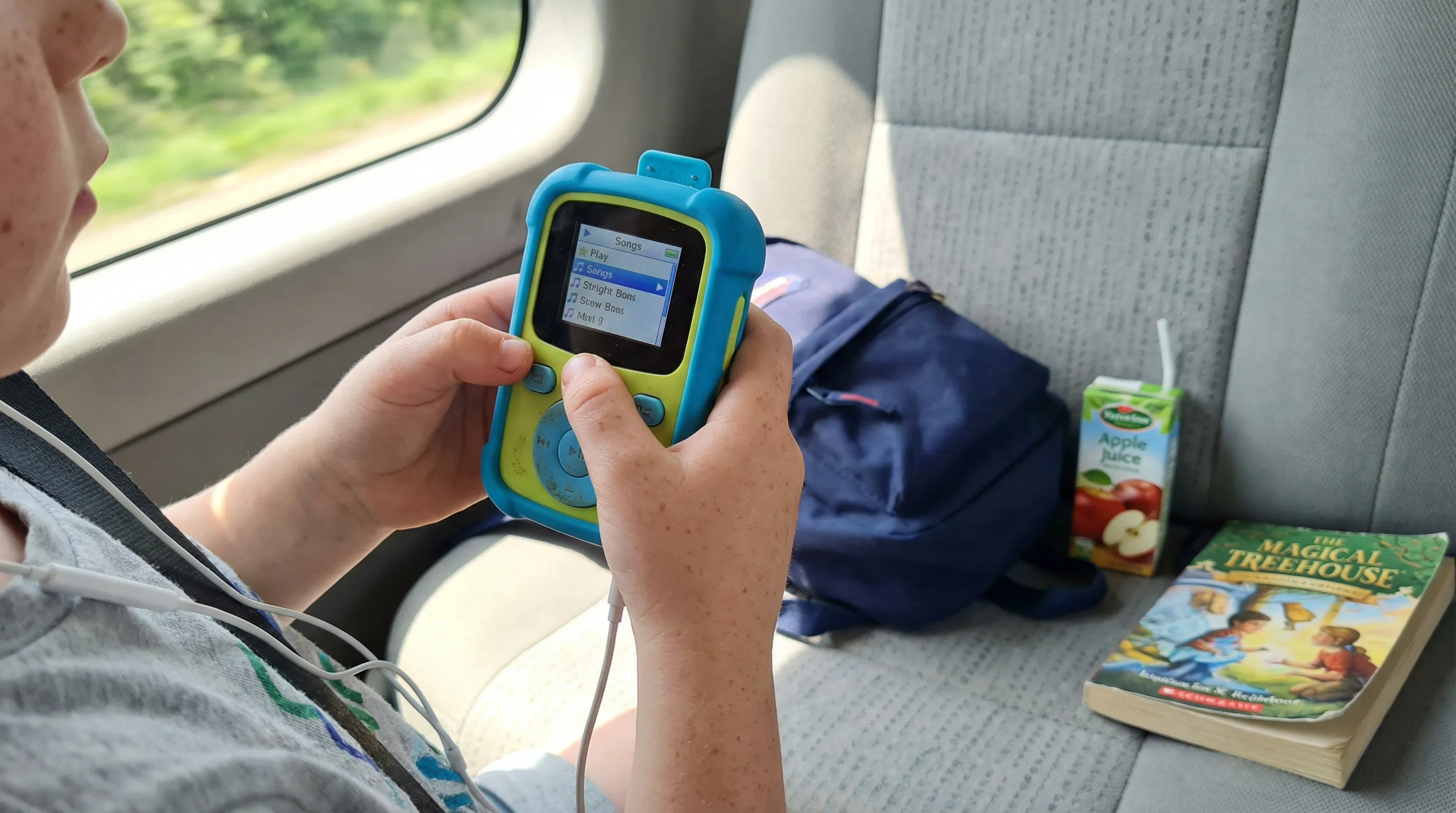 Child's hands holding a durable, clip-on MP3 player during a car ride.