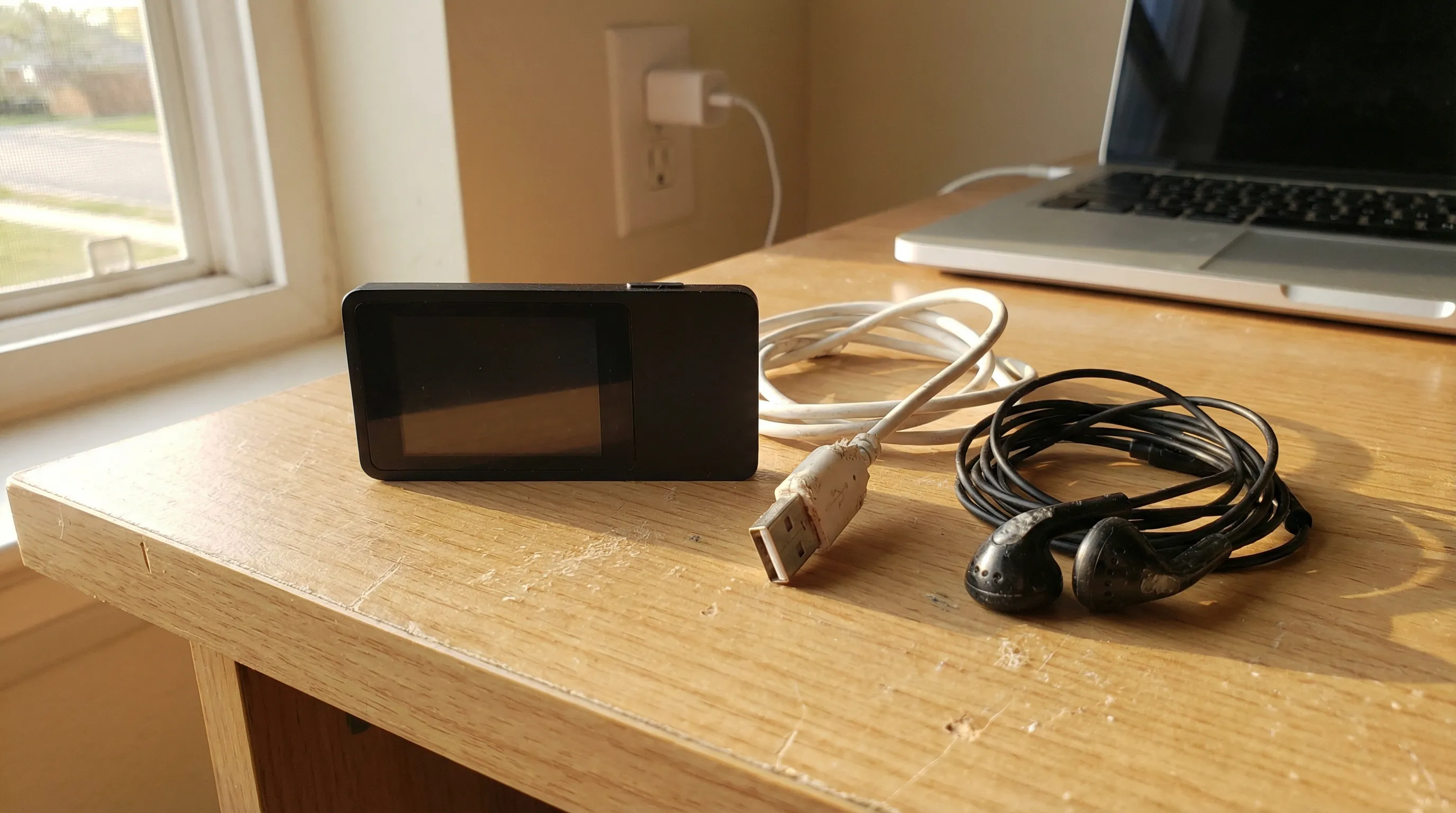 An unresponsive MP3 player on a desk beside a frayed USB cable and earbuds.