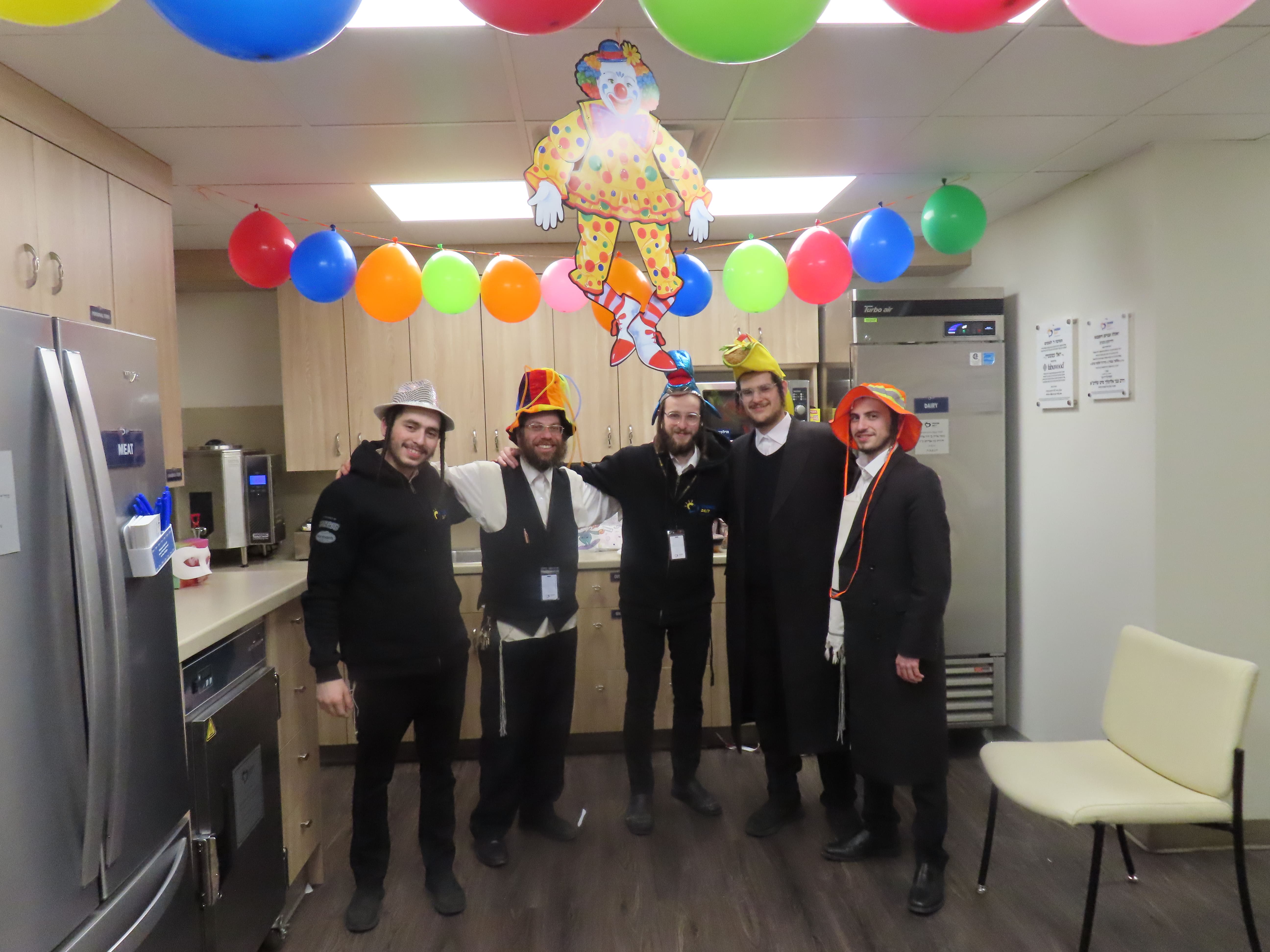 Chesed 24/7 volunteers celebrating Purim in hospital kitchen with festive decorations and costumes