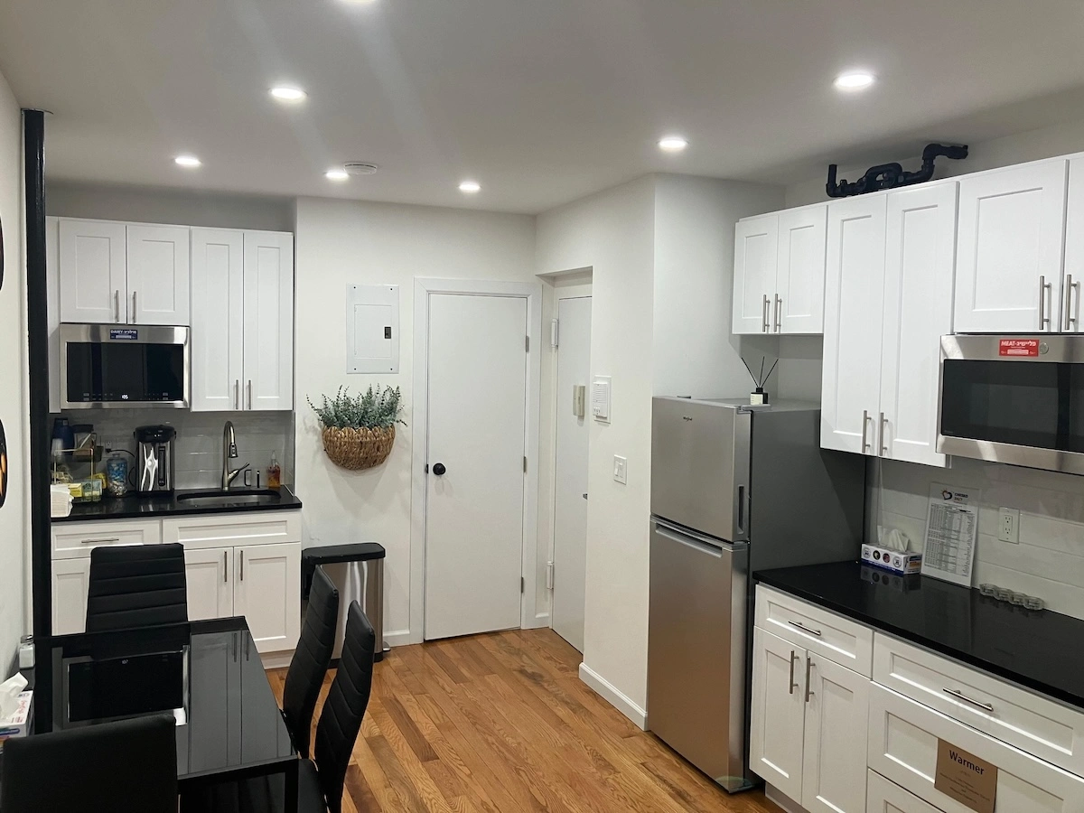 Modern kosher kitchen with white shaker cabinets, stainless steel appliances, black granite countertops, and a dining area inside a Chesed 24/7 furnished apartment near Memorial Sloan Kettering in Manhattan