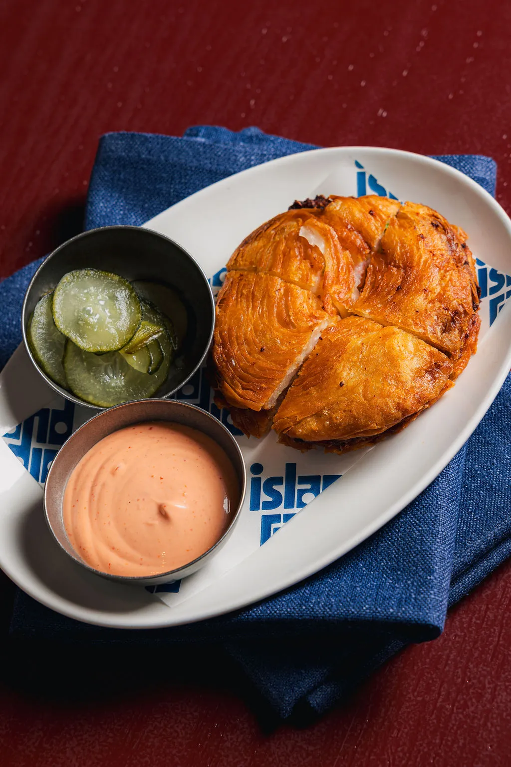 Crispy golden-brown arepa on a plate with a side of sliced pickles and pink dipping sauce.