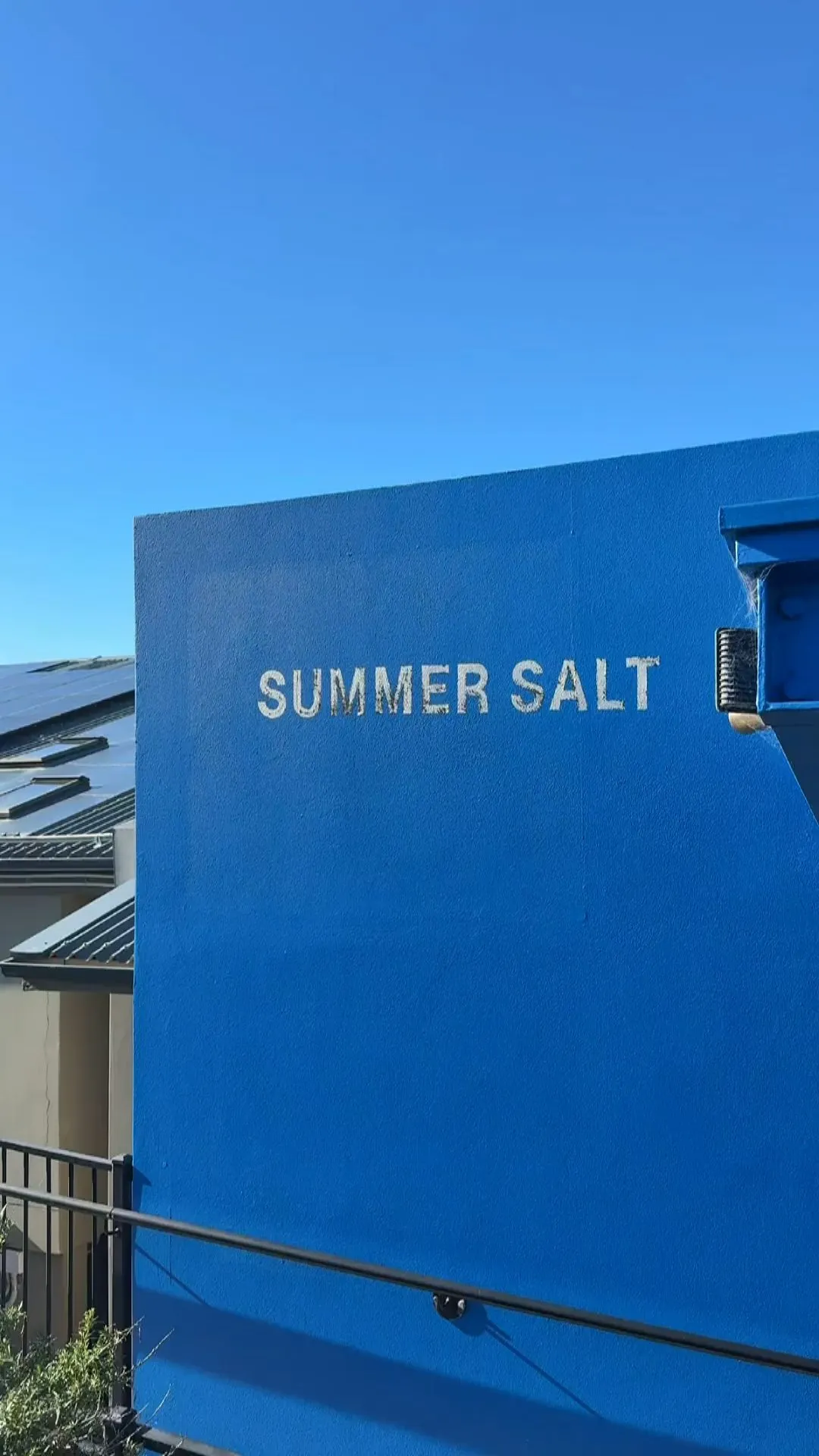 Blue exterior wall with the words 'SUMMER SALT' painted in white under a clear blue sky.
