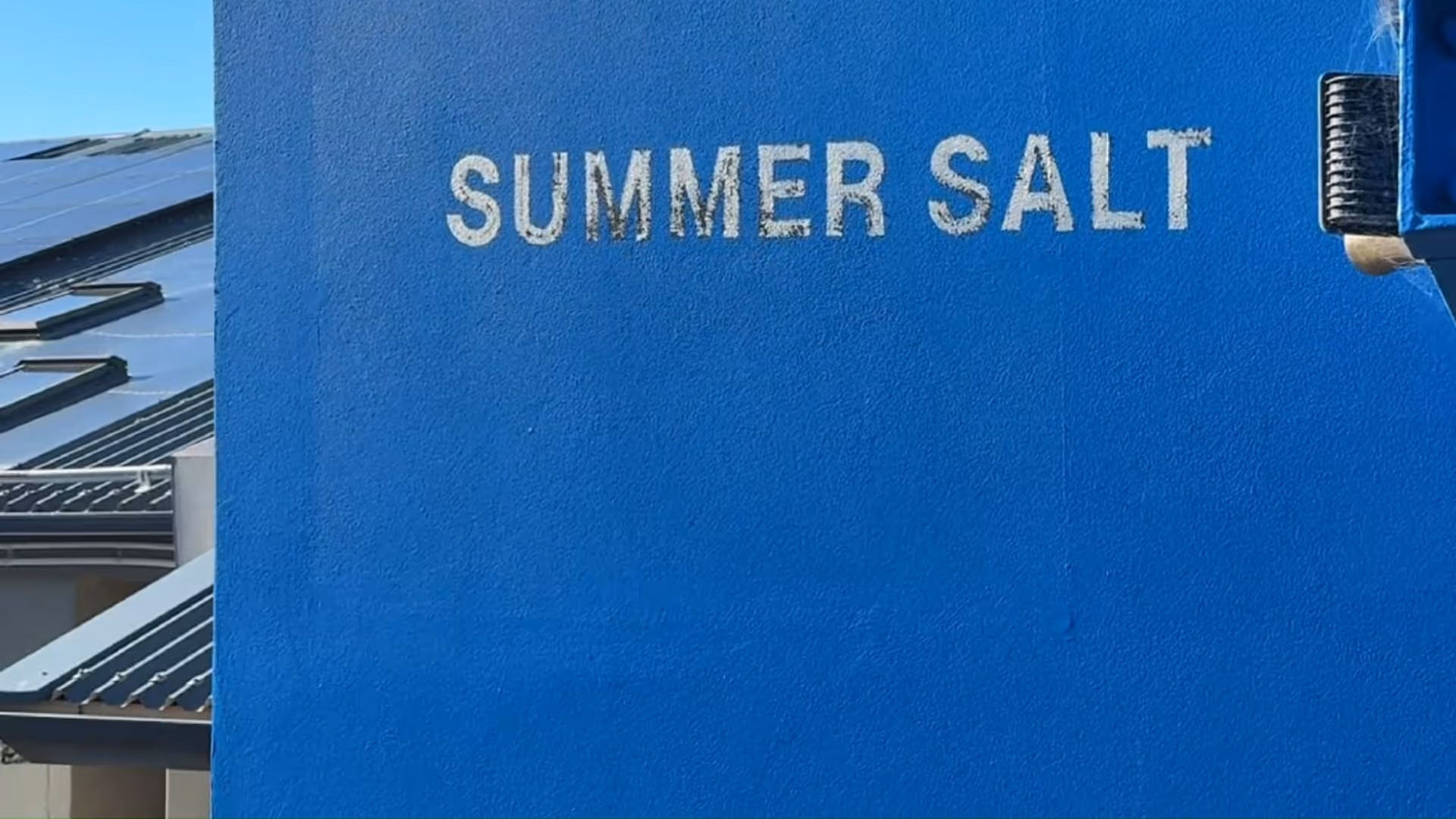Blue wall with white painted text reading 'SUMMER SALT' and part of a building roof visible on the left.